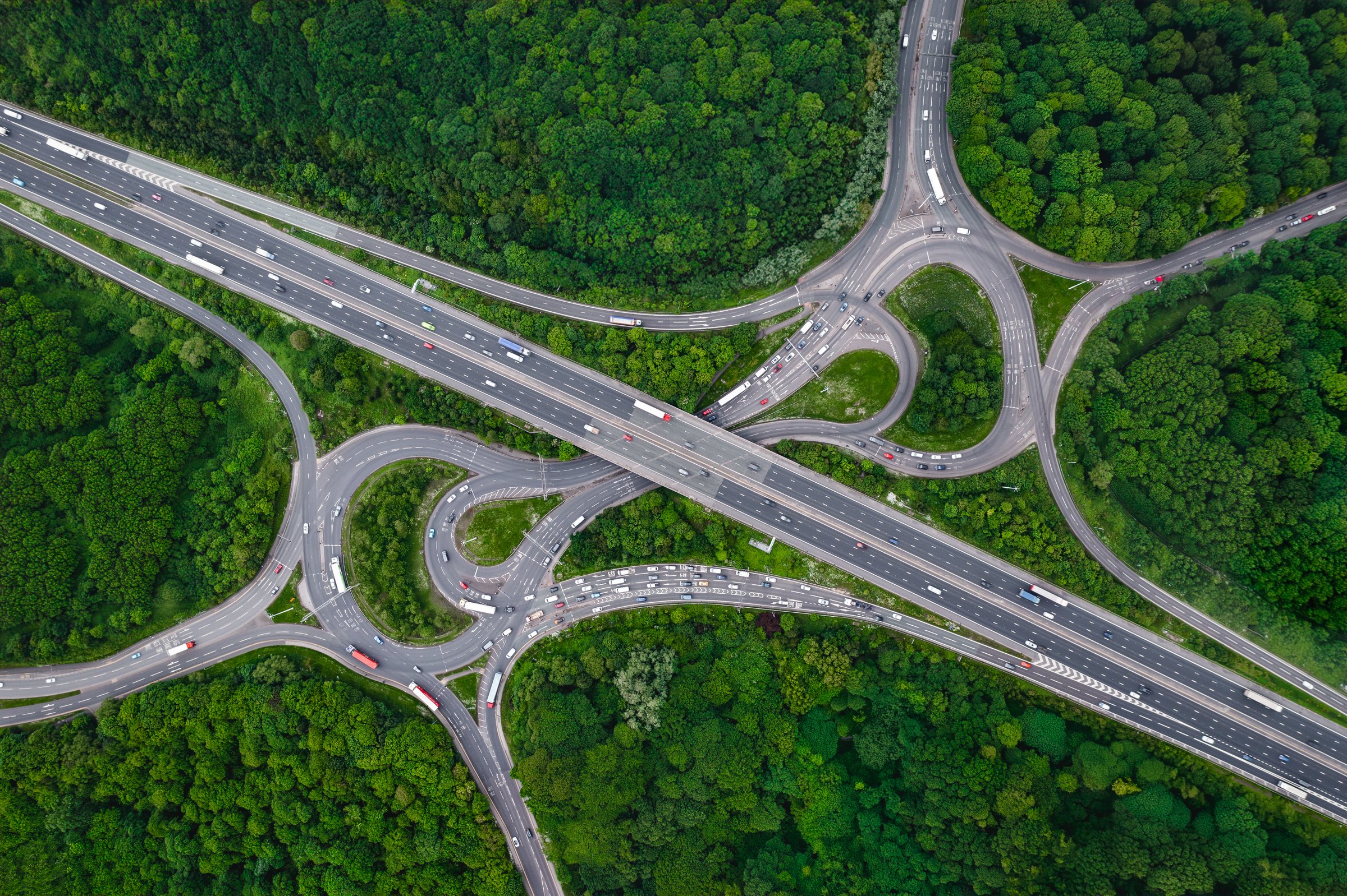 Aerial landscape view directly above a busy motorway junction cutting a swathe through dense woodland with green tree canopy providing carbon capture from exhaust fumes in an environmental concept