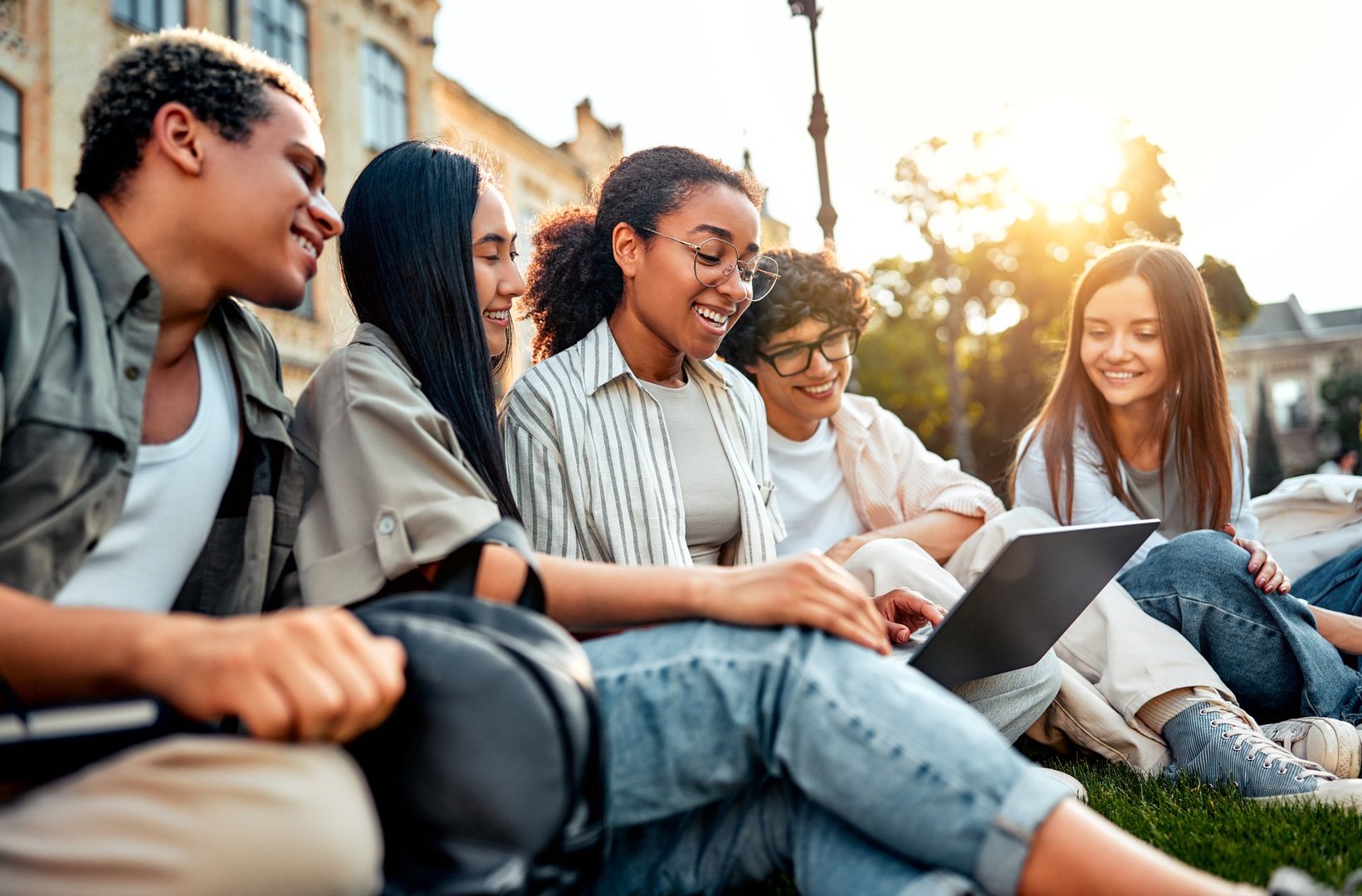 Education and study. College students sitting on grass on campus socializing, studying and spending time at leisure.