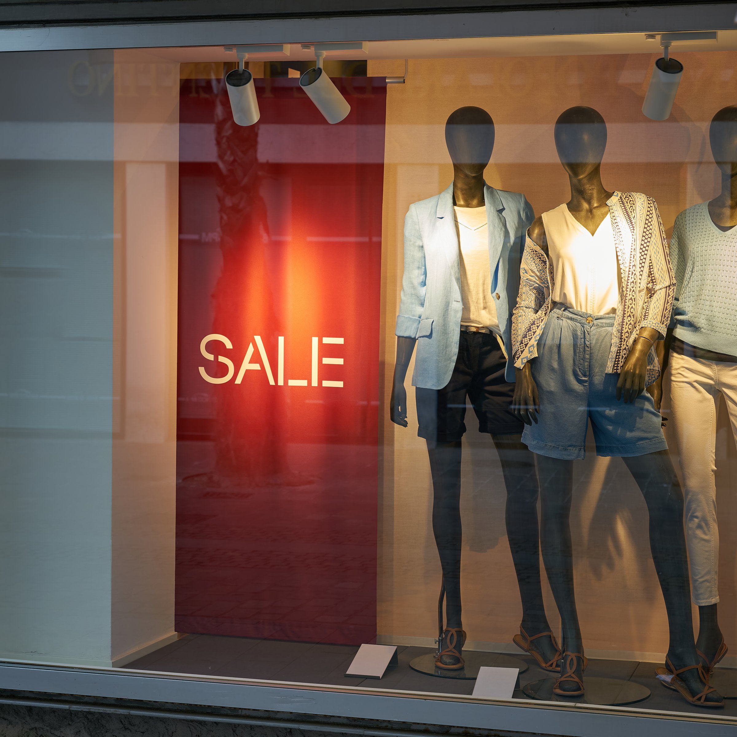 illuminated shop window with mannequins and the word Sale to indicate special offers