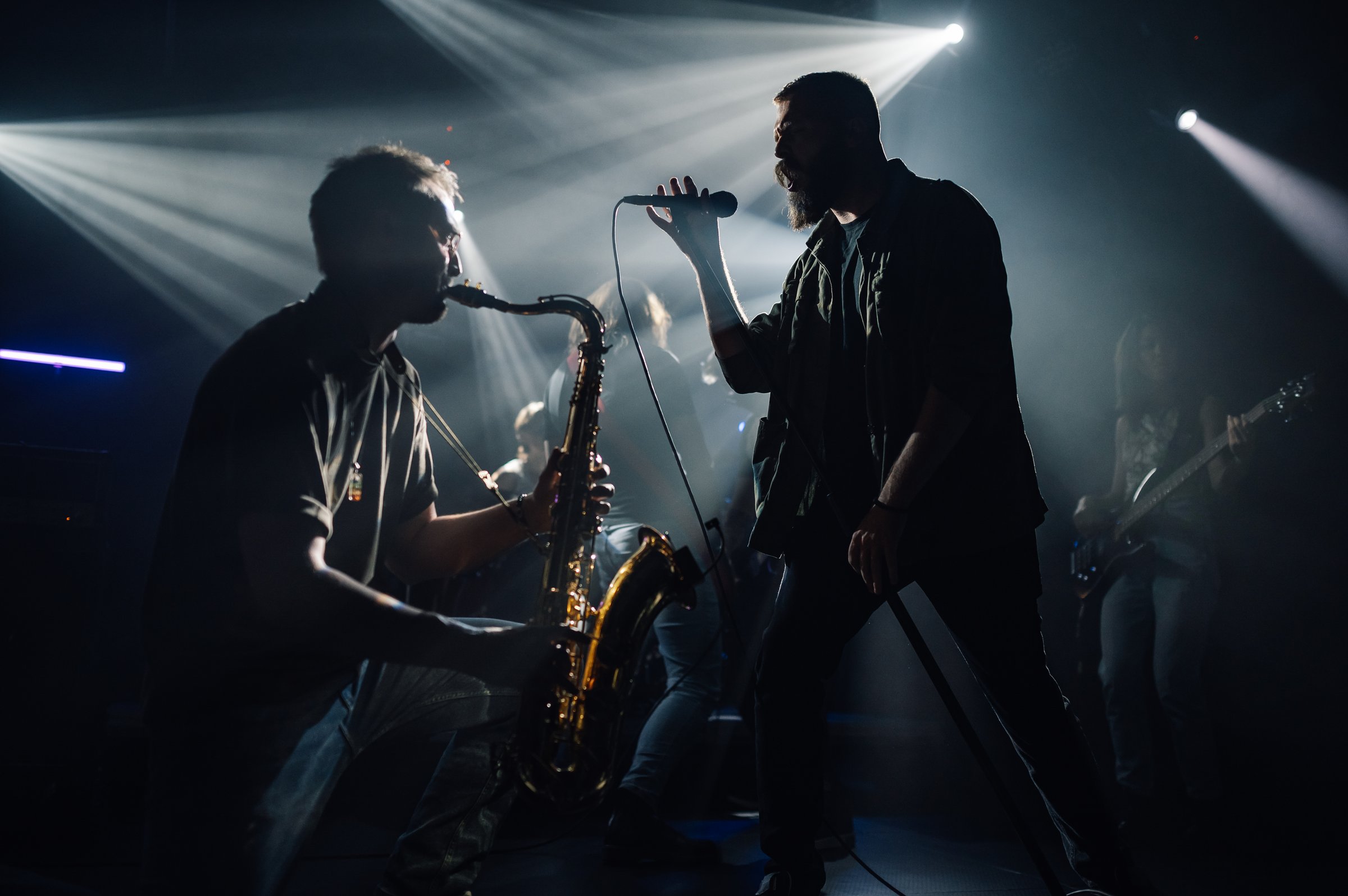 Musicians playing saxophone and singing during a live concert under stage lights, creating a vibrant and energetic atmosphere