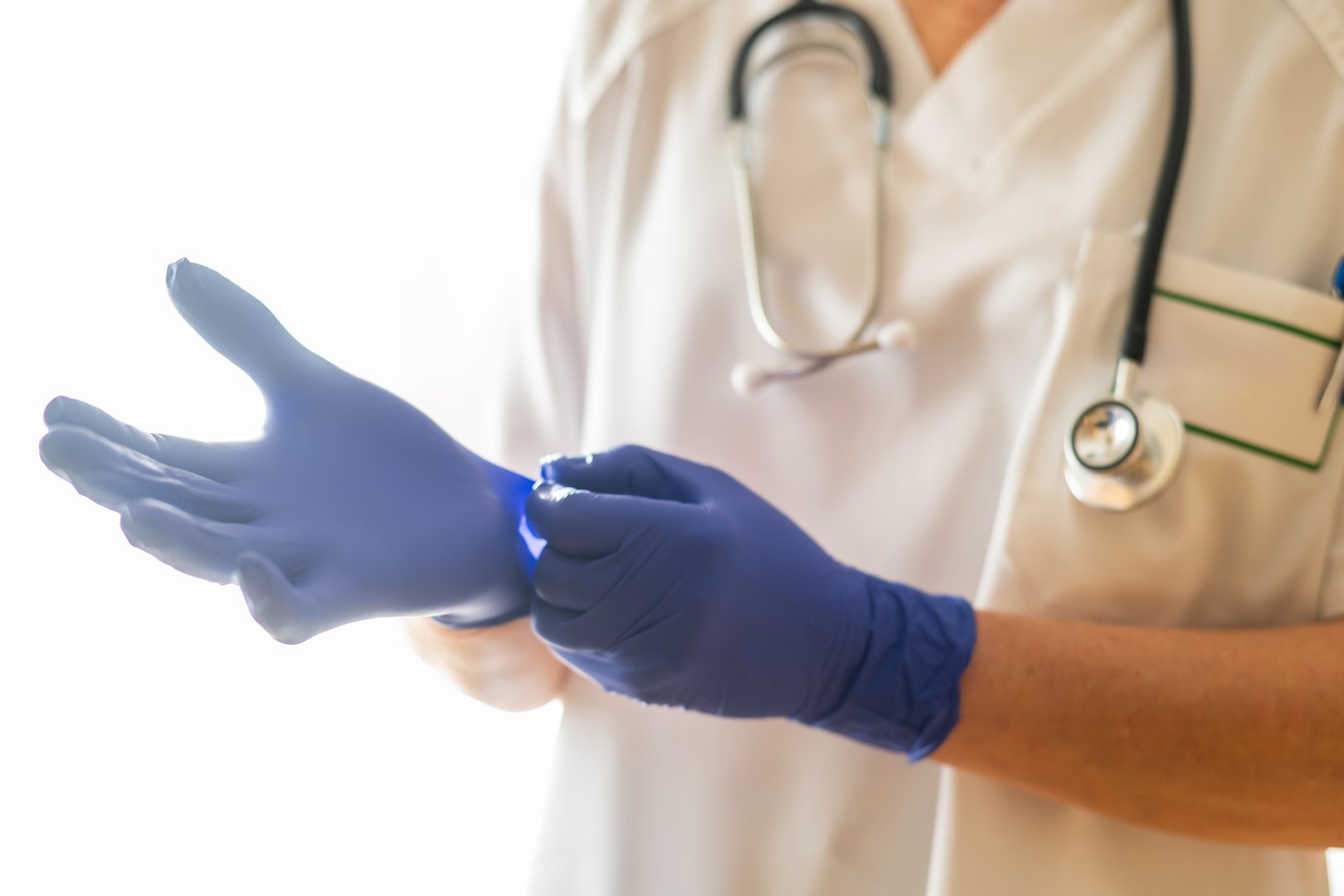 Medical professional wearing a stethoscope is putting on blue nitrile gloves, preparing for a medical examination or procedure, emphasizing hygiene and patient safety in healthcare