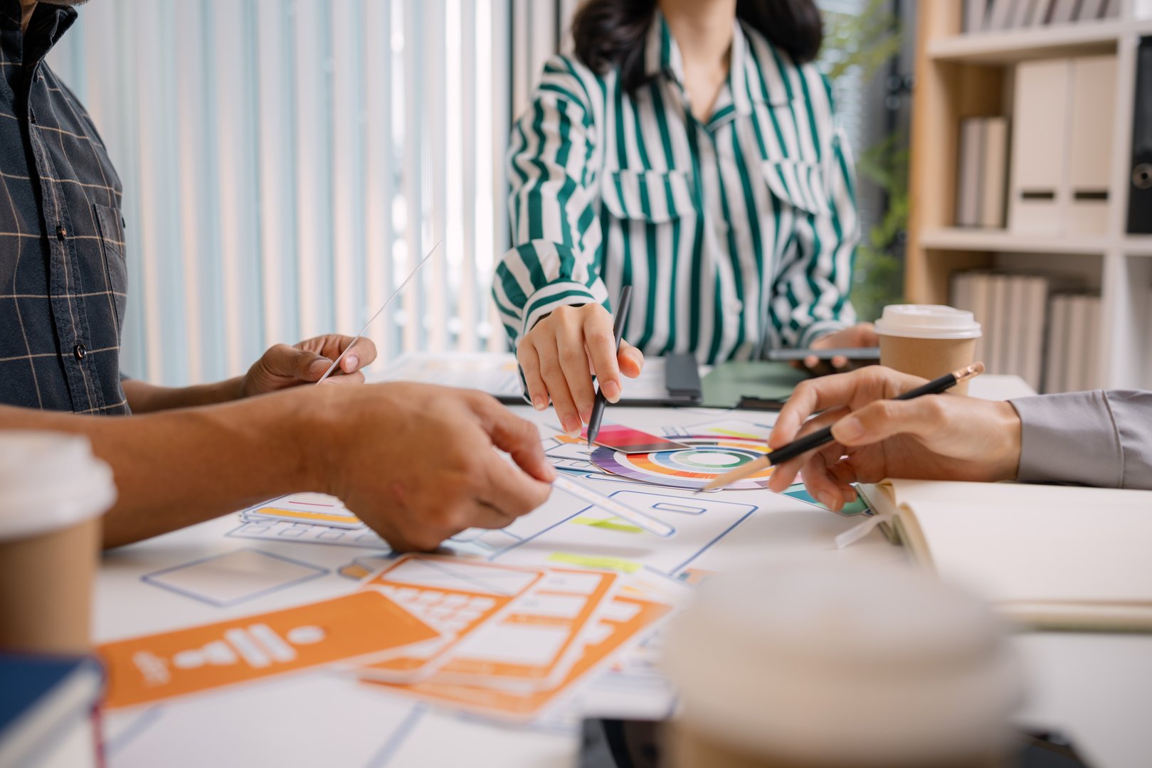 A group of UX/UI designers brainstorming creative ideas together, discussing color palettes and layout concepts for a new mobile application interface in a modern design office.