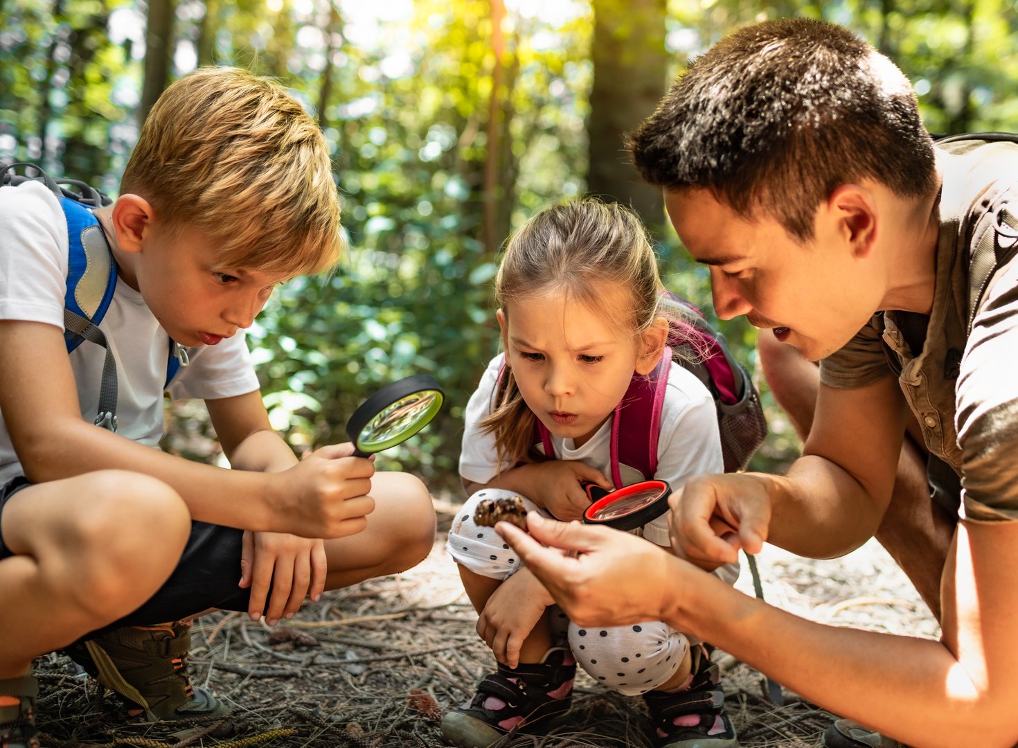 Father and his children boy and girl exploring nature through a magnifying glass.