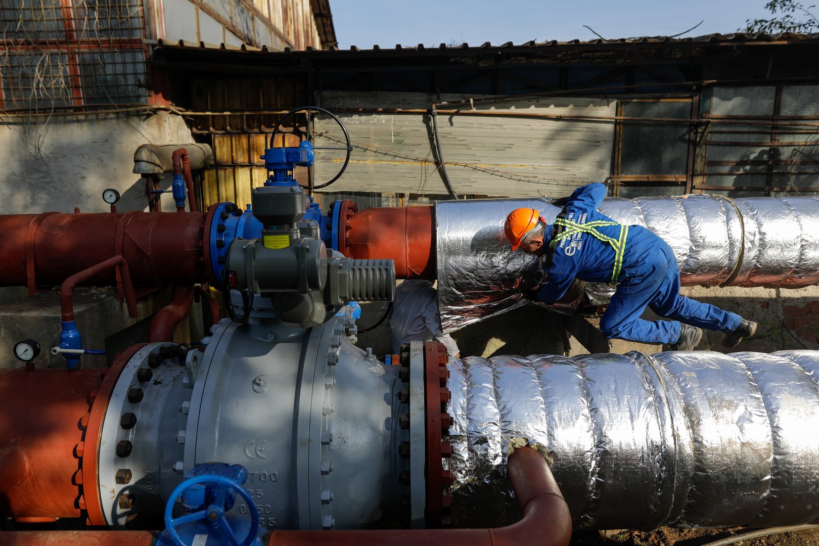 Worker uses glass wool to thermal insulate a hot water metallic pipeline