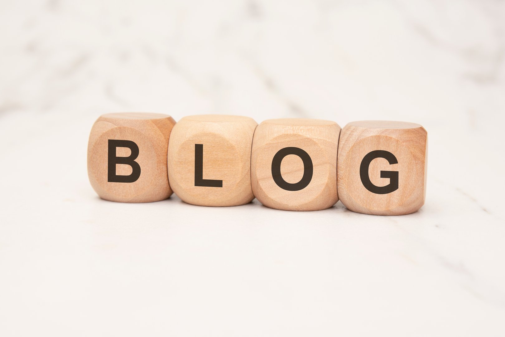 four wooden cubes with bold black letters spelling BLOG on a light marble surface. image represents blogging, digital content creation, and online publishing in a modern and minimalistic style