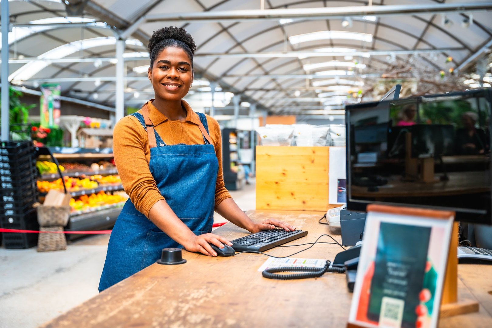 Portrait of a young grocery store employee smiling while standing at the checkout counter, ready to assist customers