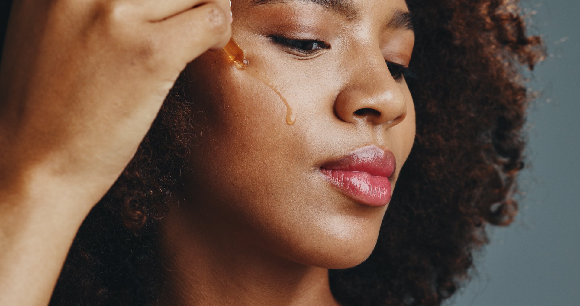 Dropper, skincare or African woman with serum for beauty, shine or facial glow isolated on studio background. Face, cheeks or model with oil moisturizer for collagen, vitamin c cosmetic or benefits