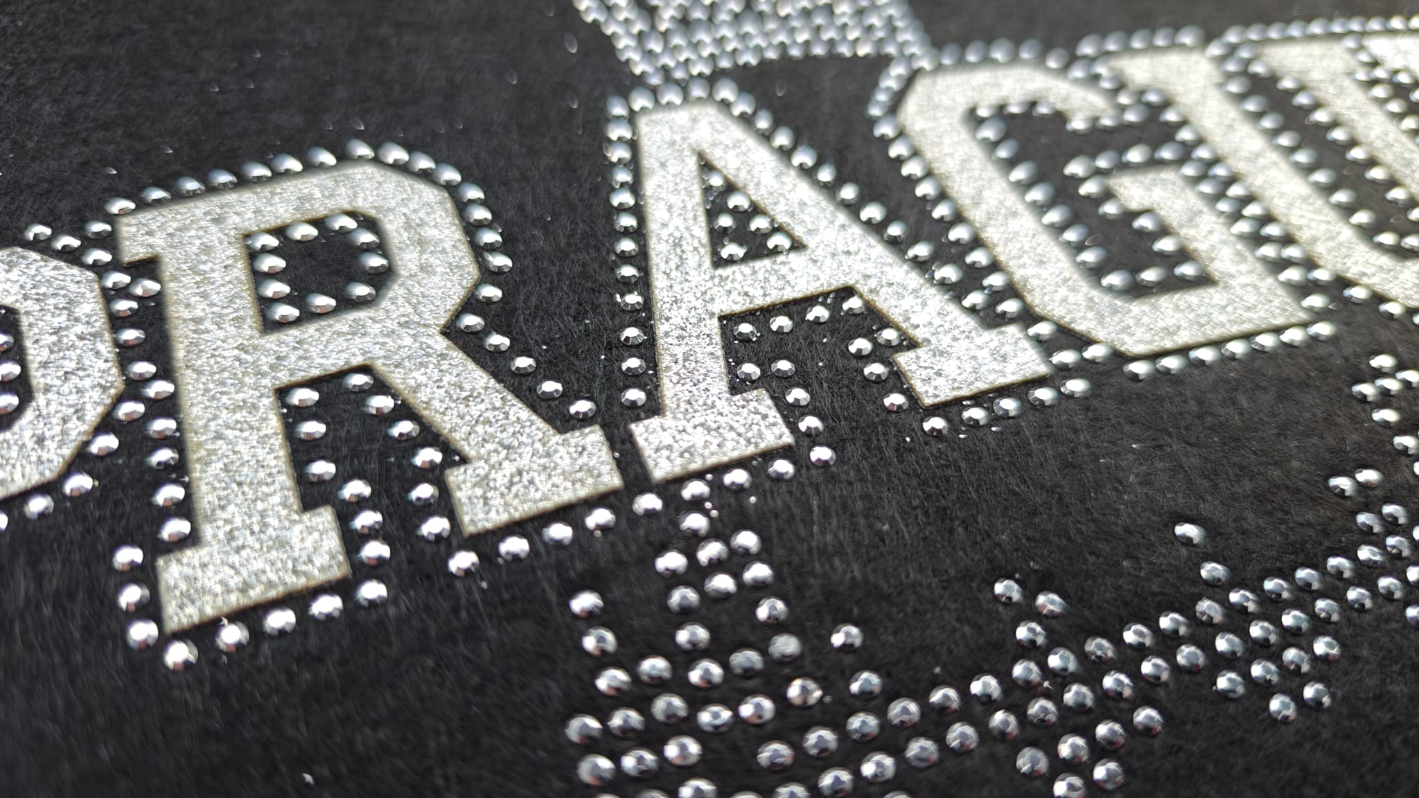 Close-up of the word PRAGUE on black fabric, embellished with shiny silver beads and rhinestones.