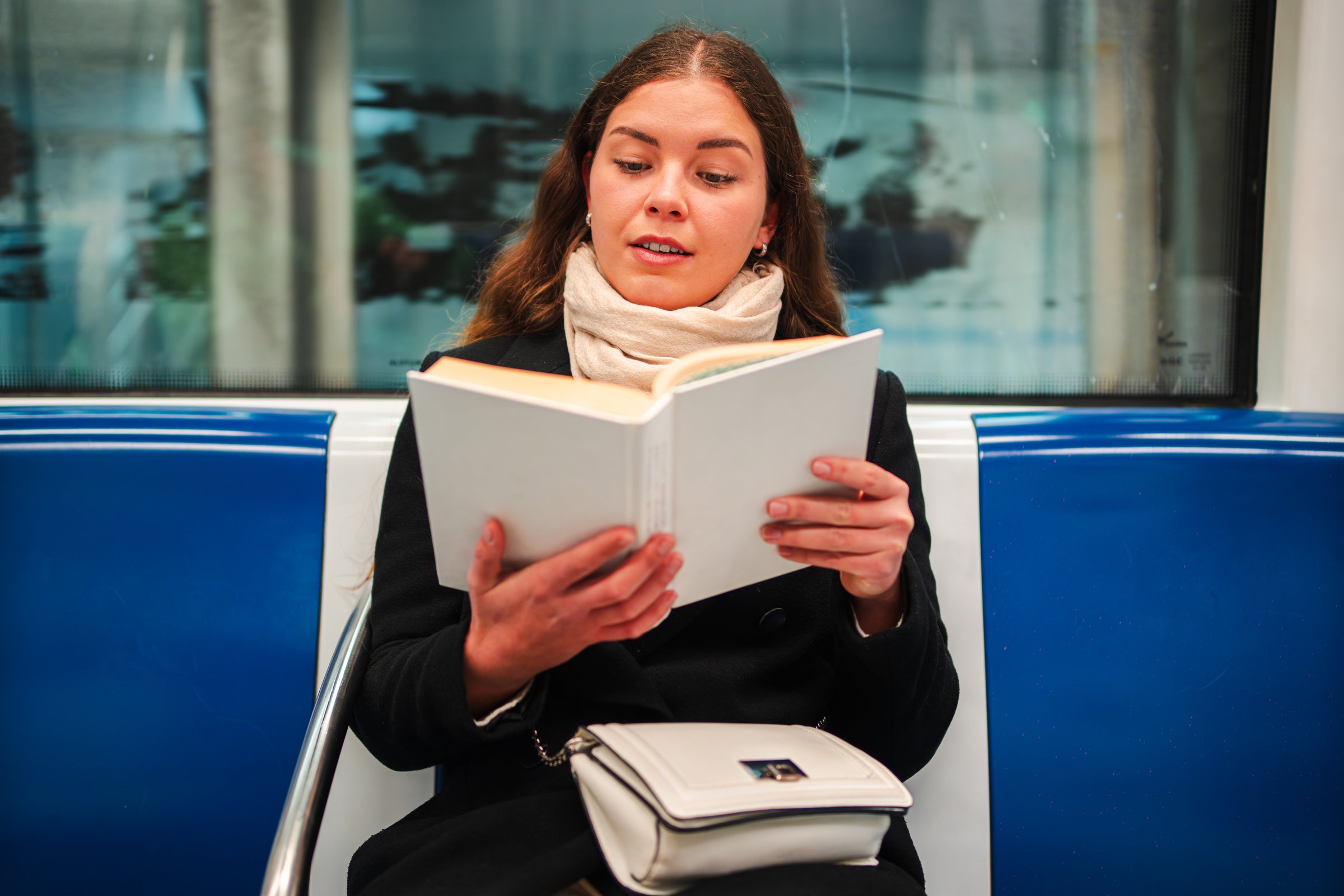 A focused woman deeply engaged in reading an interesting book while using public transport, highlighting her passion for literature and the joy of getting lost in a captivating story during her commute