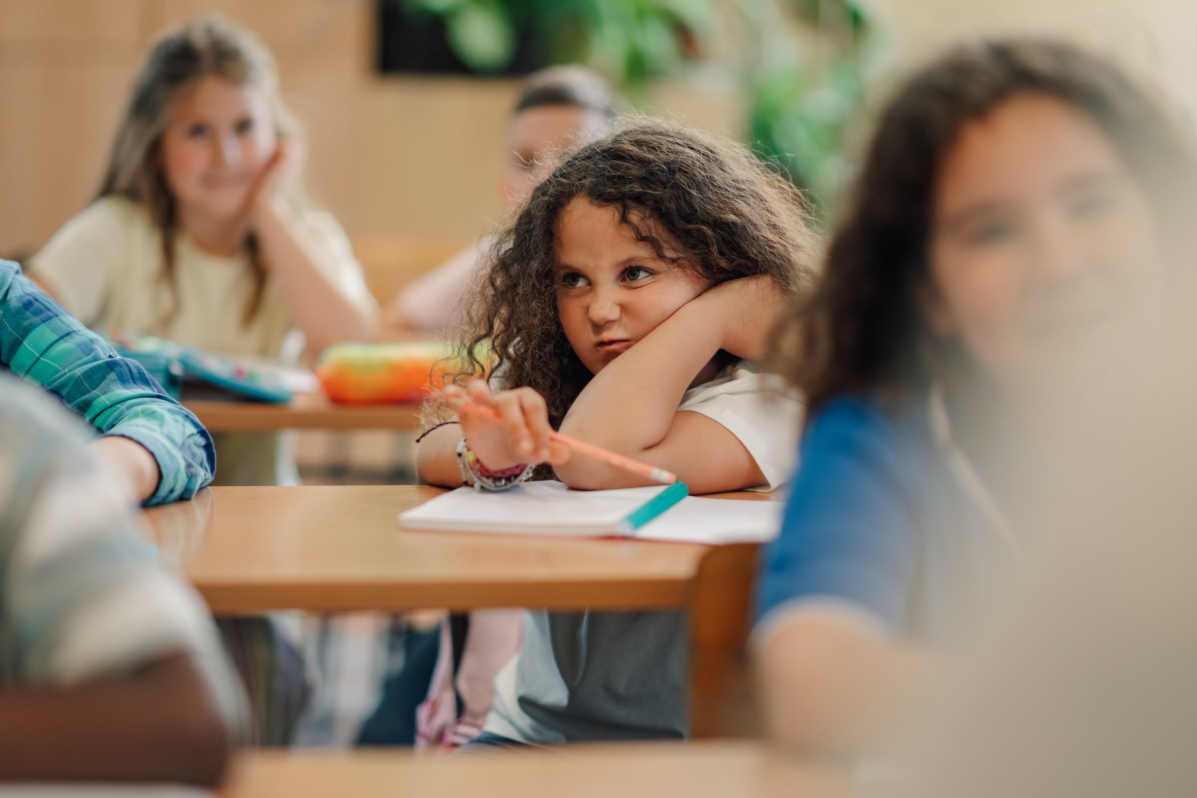 Bored elementary school student looking away during class, feeling uninterested and restless while sitting at her desk