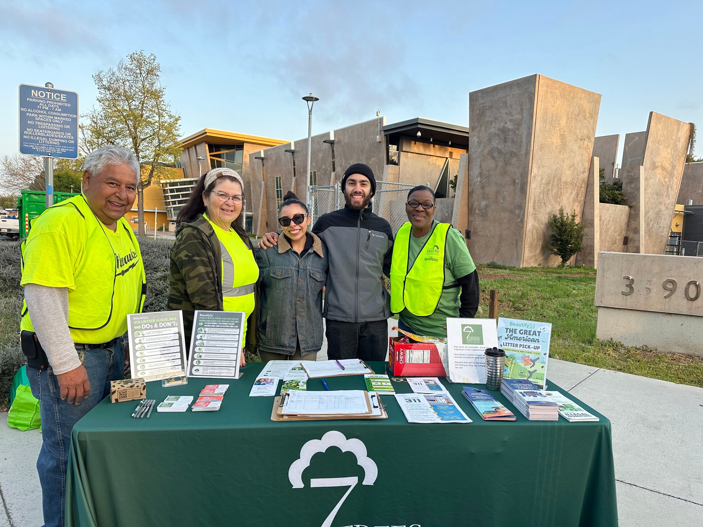 Group of five people at an outdoor event booth with pamphlets and informational materials on a table.