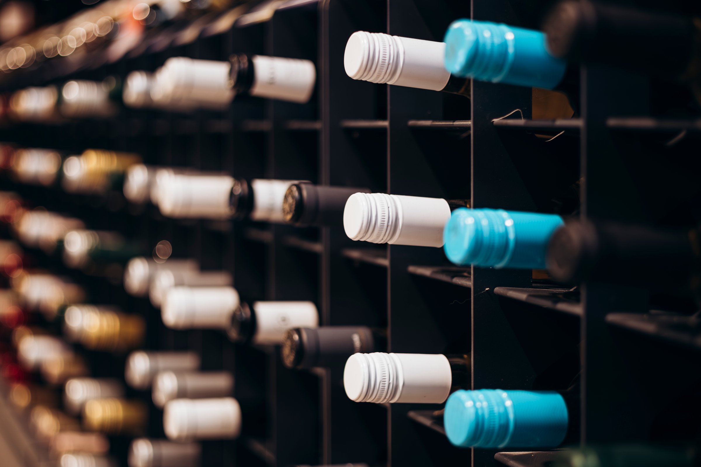Wine bottles in vertical shot stacked on racks shot with limited depth of field. Red wine on shelf. Wine bottles lined up and stacked on shelves in a luxury private collection collectible wine store.