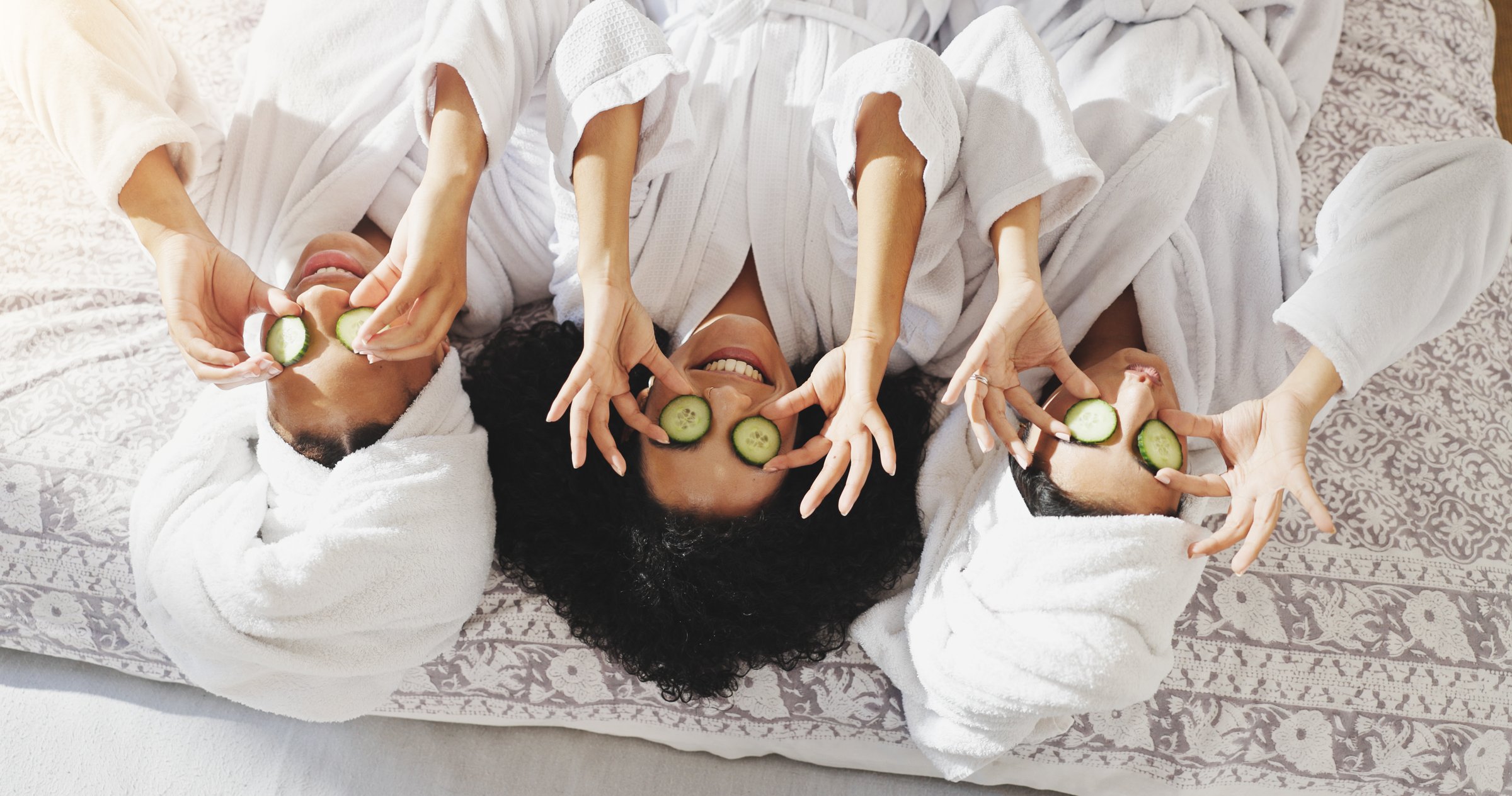 Spa, cucumber and smile with friends in hotel for beauty treatment, bonding and hospitality. Skincare, facial and upside down with women in bedroom of resort for self care, pamper and travel