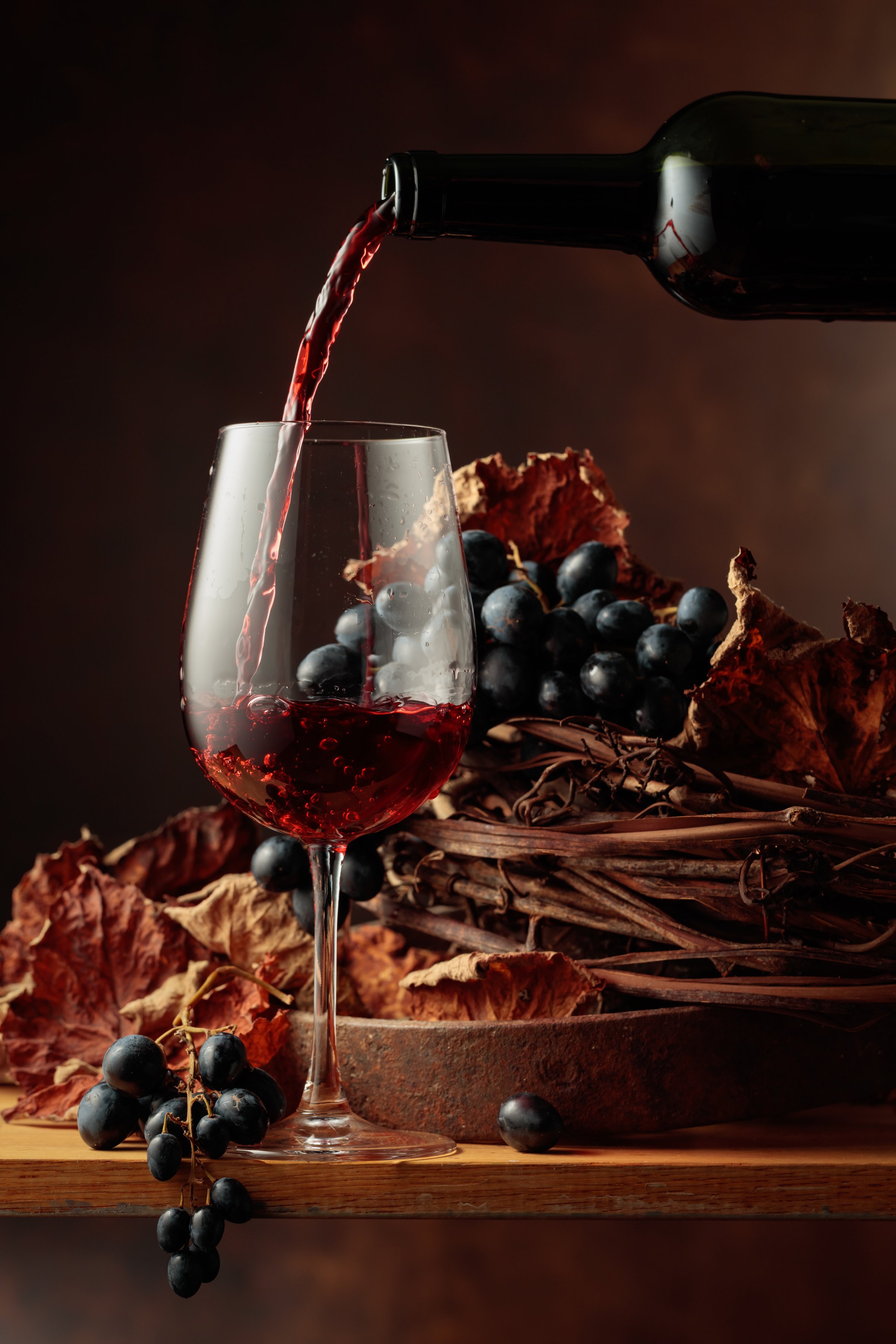 Wine is poured into a glass. Red wine and bunch of grapes on vintage wooden table.