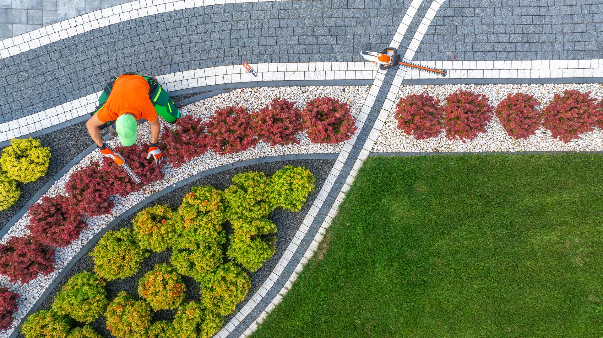 Aerial View of Garden Worker Pruning Small Driveway Area Plants. Landscaping Industry Theme.