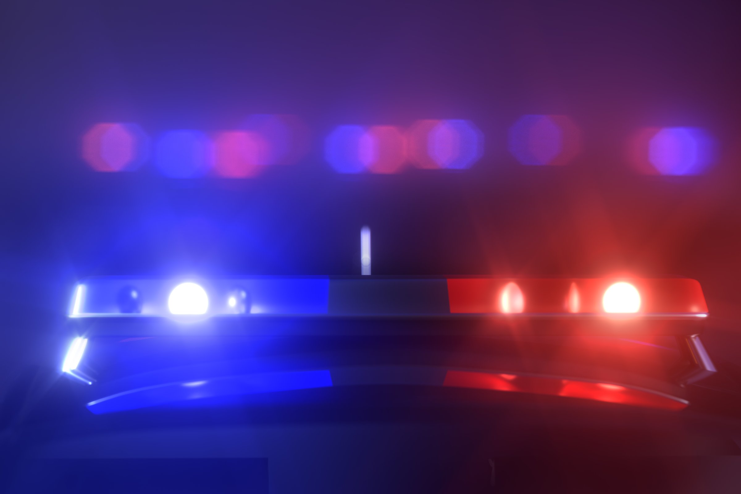 Closeup of a police car siren with flashing red and blue emergency lights in the dark night. Focus on light reflection, bokeh and lens glow creating tense law enforcement atmosphere