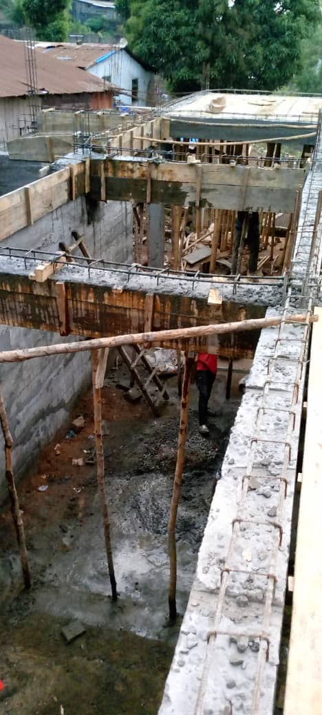 Concrete slab with steel rebar reinforcement in construction site, surrounded by walls and a corrugated metal roof structure.