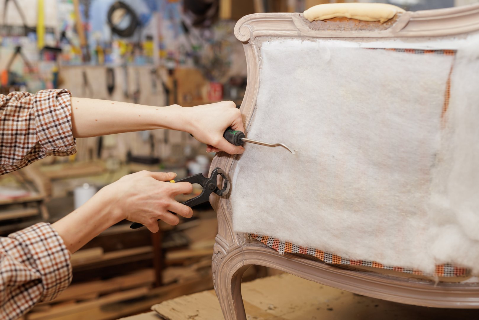 Female restorer using tools to repair vintage chair upholstery in workshop, showing detailed furniture restoration process