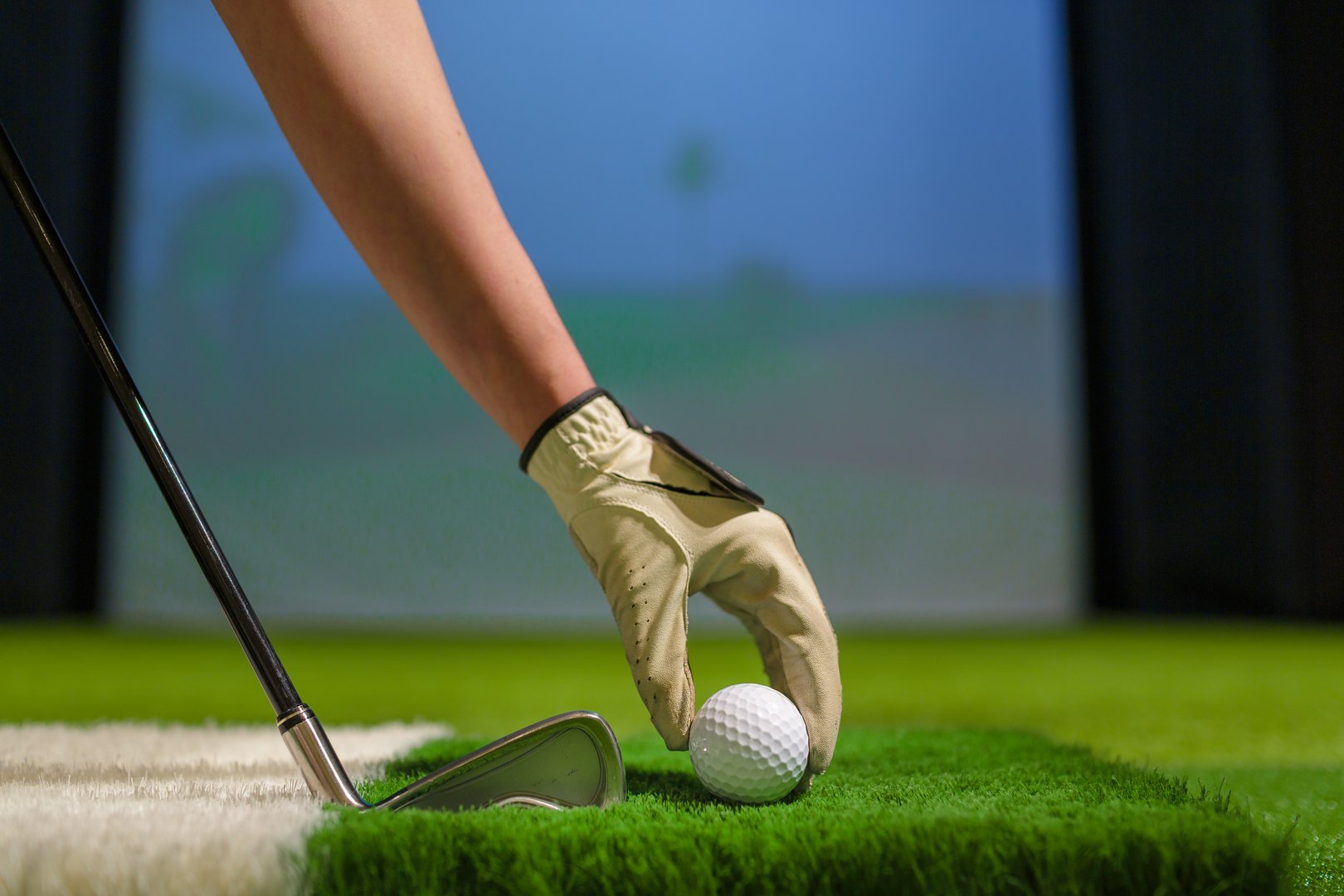 Golfer hand with glove places ball on artificial grass in modern indoor golf simulator during training or practice session