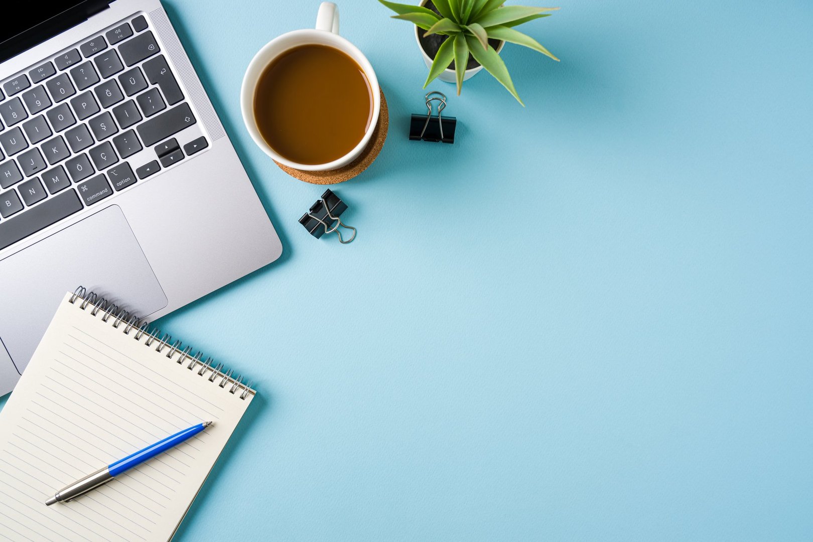 Coffee cup, laptop keyboard and various stationery items on blue office desk. Business office concept