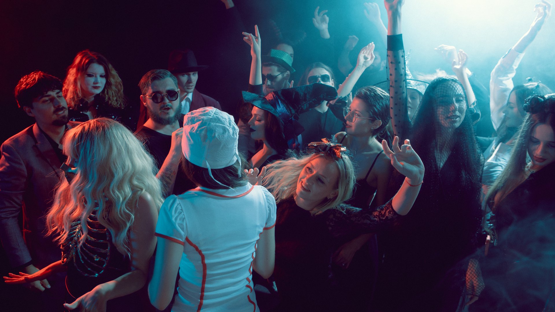Crowd of young people celebrating at Halloween party with costumes and smoky lights. Concept of entertainment, social lifestyle, fashion branding and music culture advertising.
