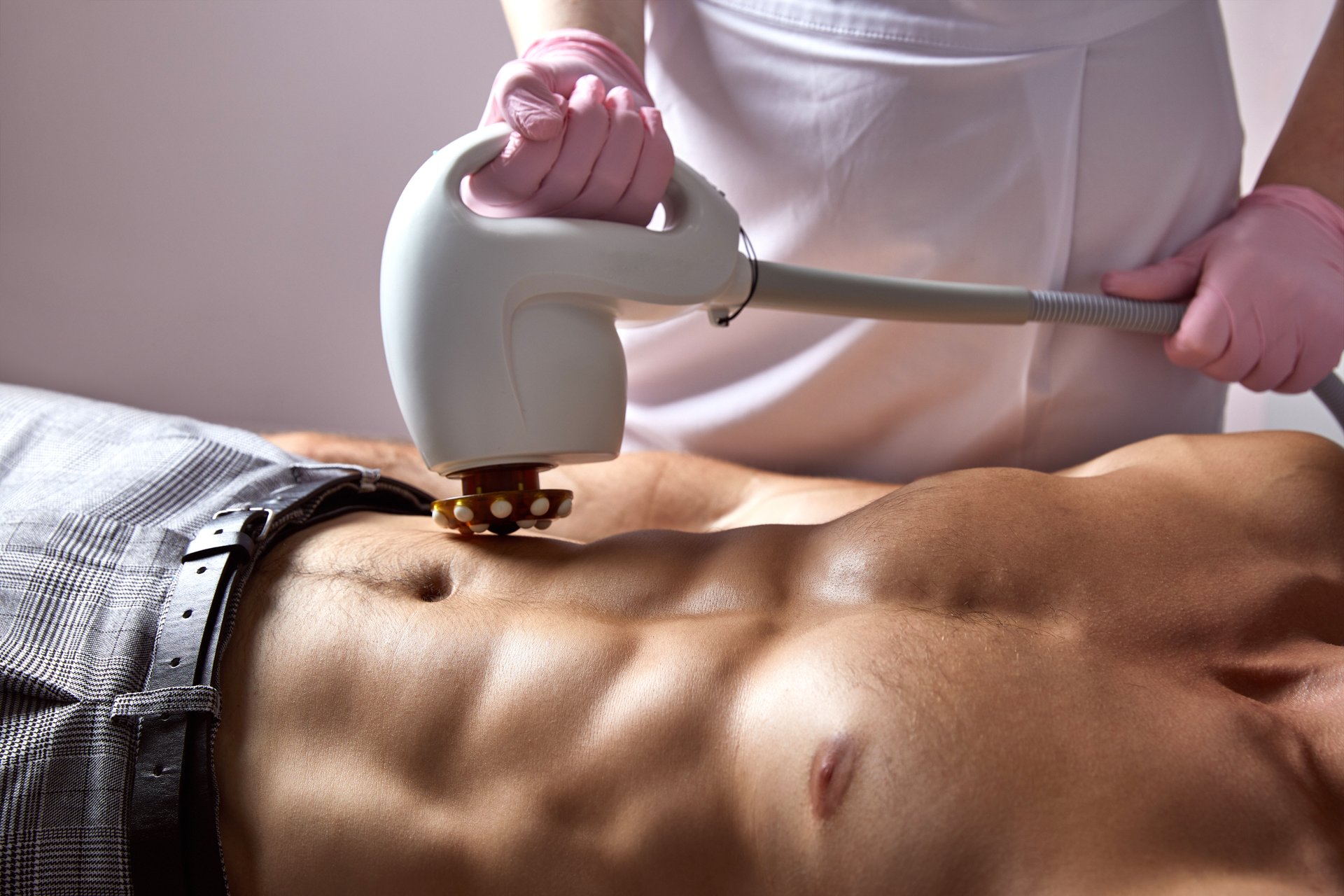 Man receiving fat reductive skin lifting body treatment on modern equipment at cosmetology clinic, male body care concept