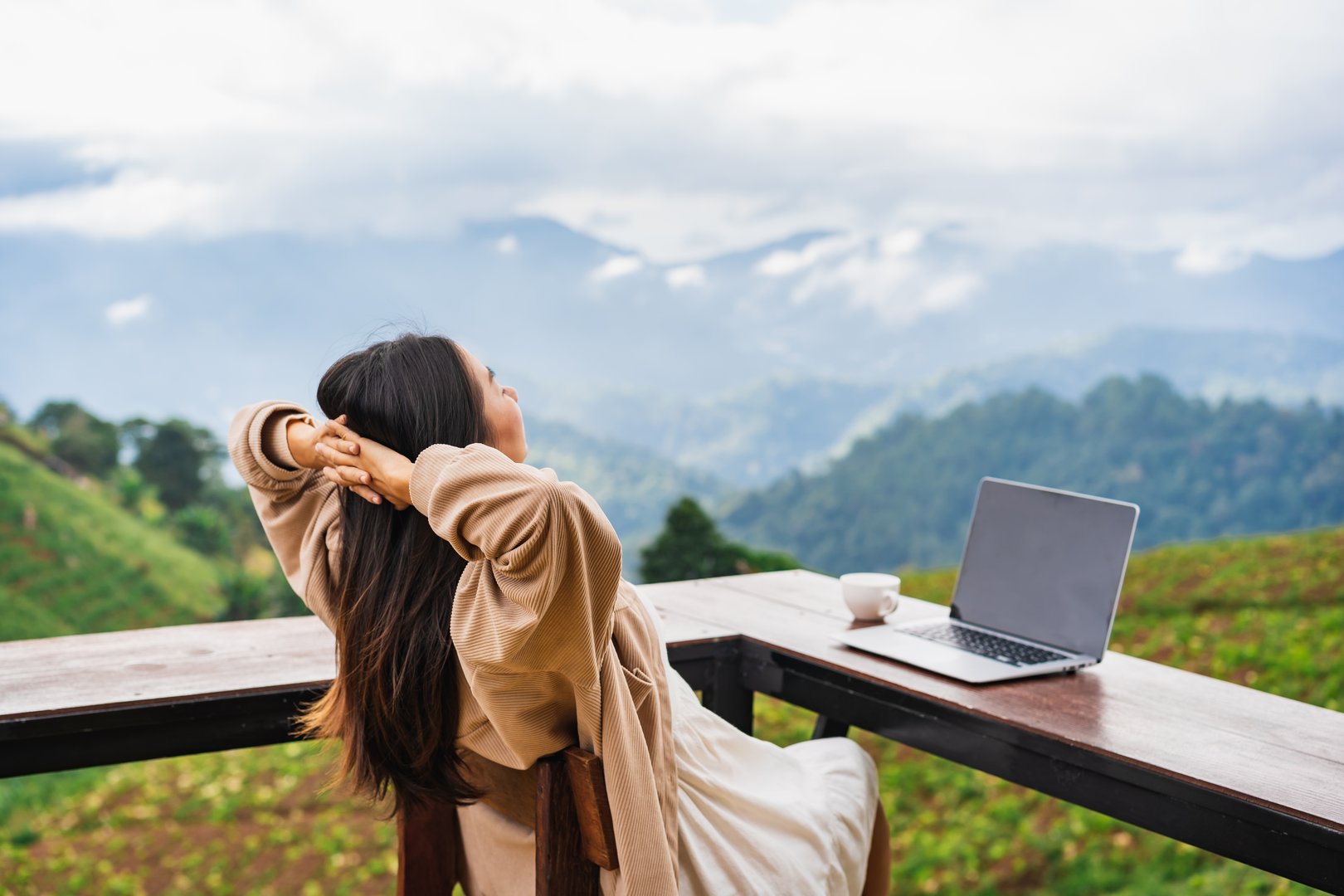 Young woman freelancer traveler working online using laptop and enjoying the beautiful nature landscape with mountain view