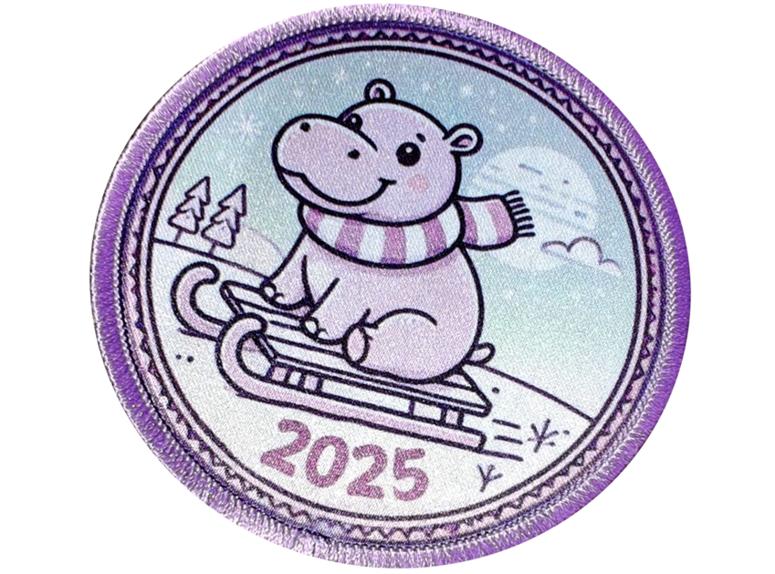 A round patch depicting a smiling hippo wearing a scarf, sledding down a snowy hill, with 2025 written at the bottom.