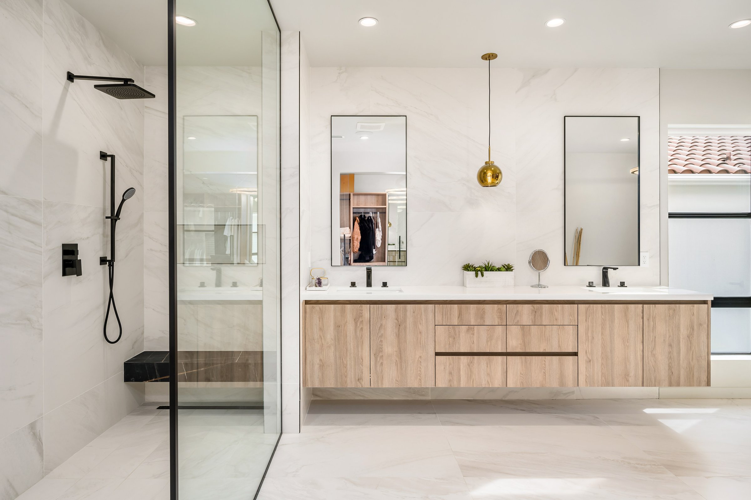 A bathroom with twin sinks, marble countertops, and glass shower enclosures