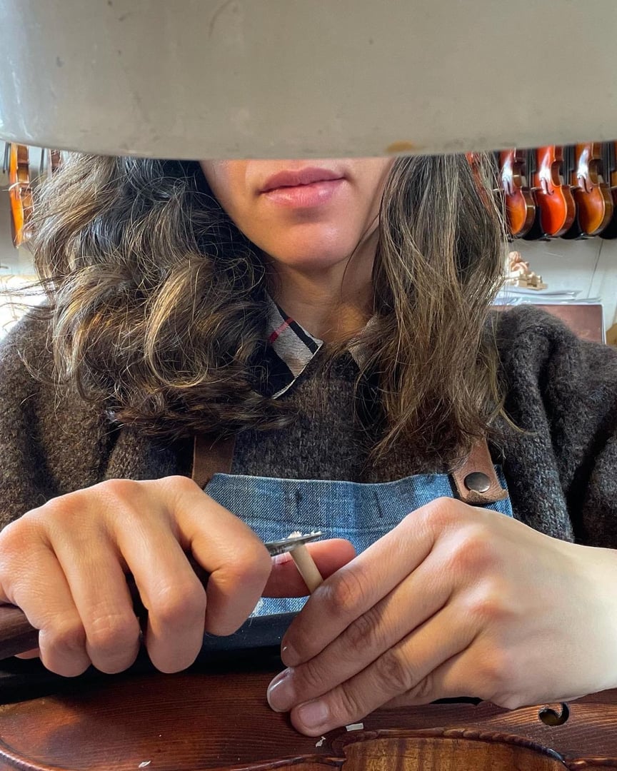 A woman carefully polishes a violin, showcasing attention to detail in string instrument maintenance. Her gentle touch and the warm setting bring an intimate and serene atmosphere to the scene.