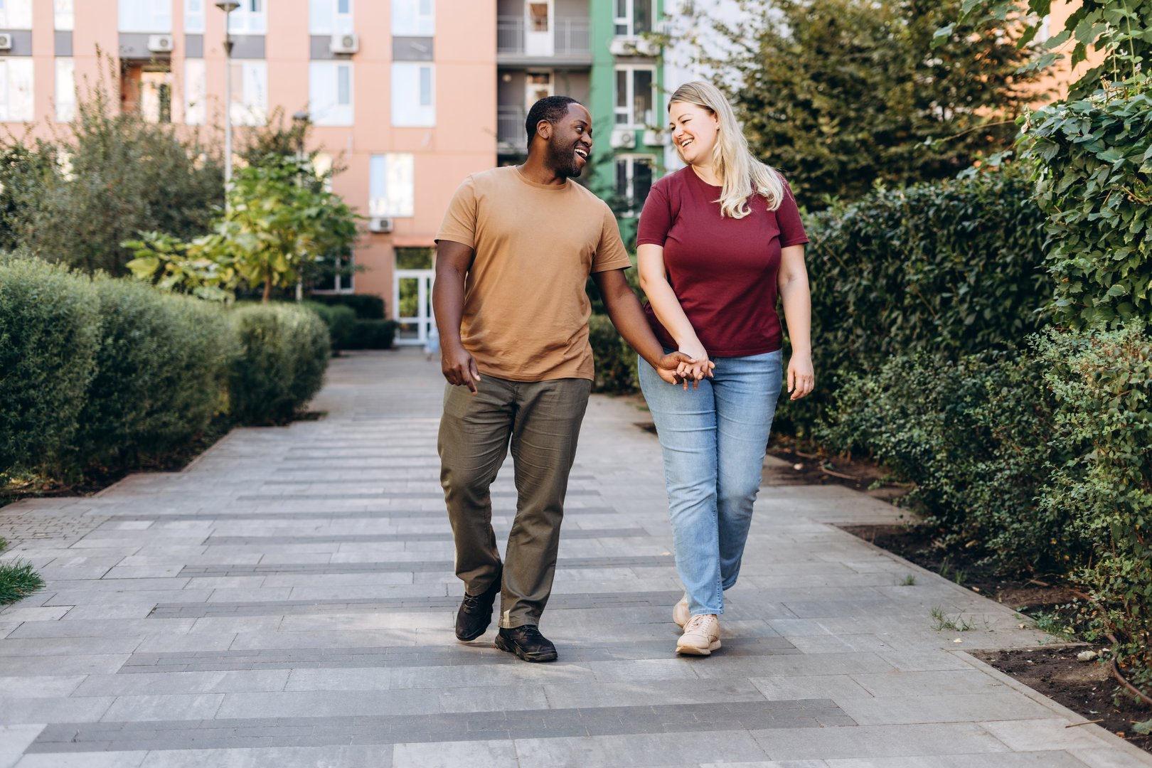 Smiling romantic multiracial couple looking each other dating holding hands, walking in the city outdoors