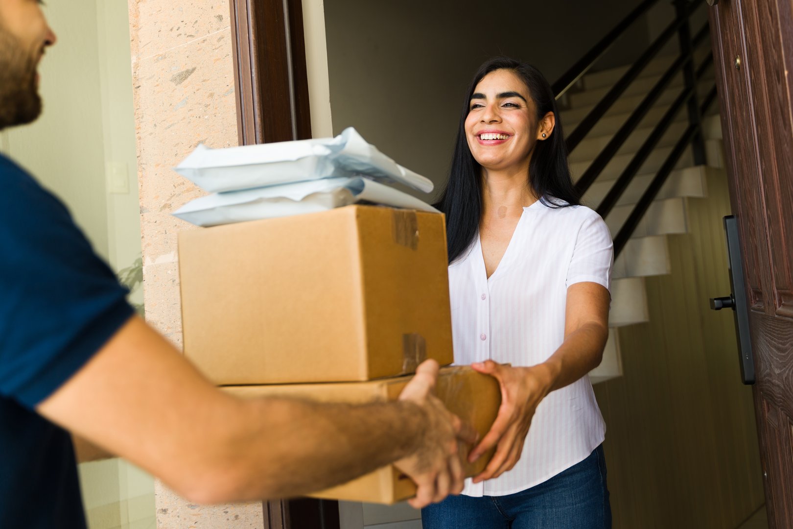 Smiling woman receiving a stack of packages from a delivery man at her front door