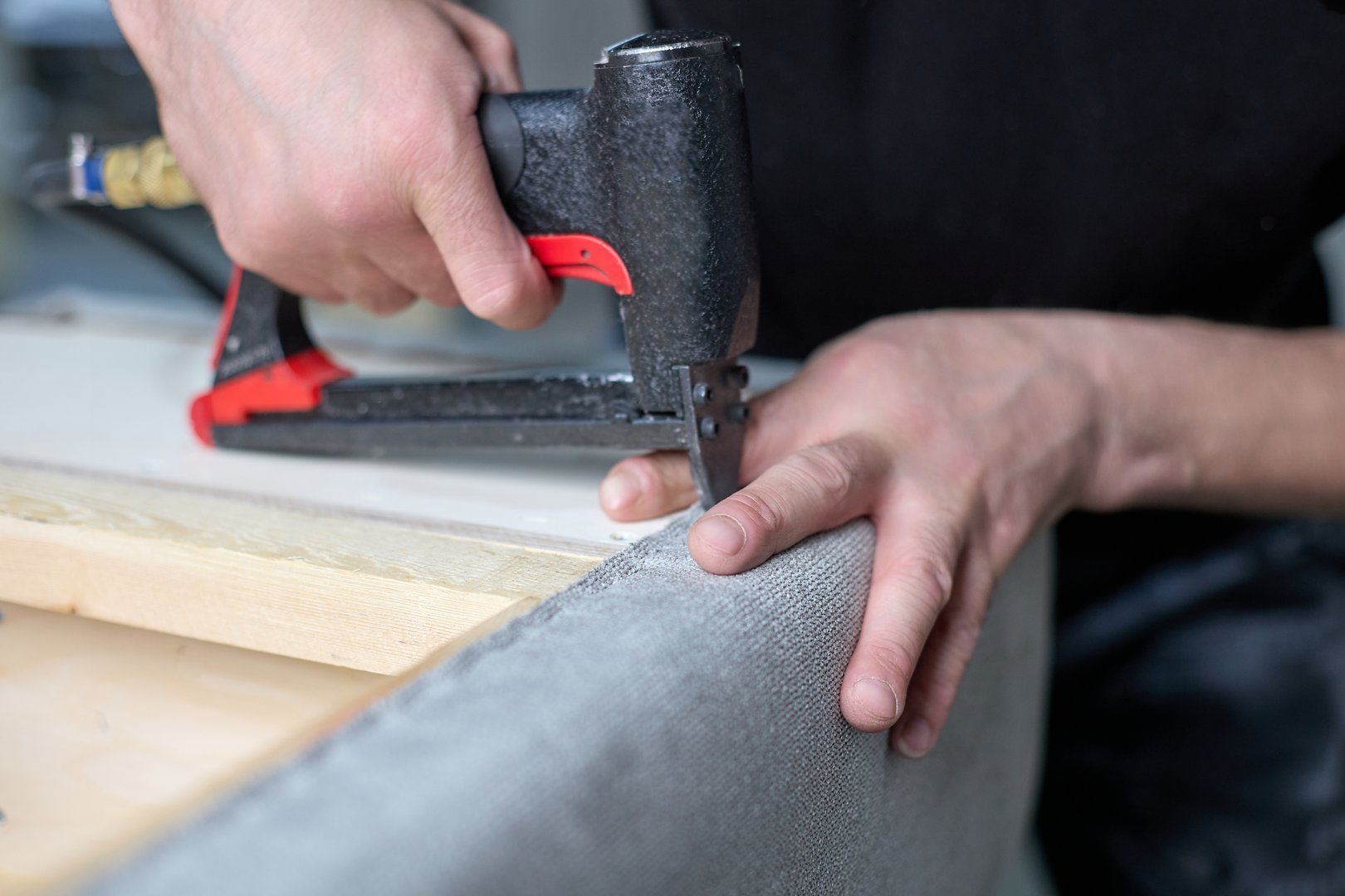Worker qualitatively fixes the fabric with a pneumatic stapler on the body in the factory shop. Production of upholstered cabinet furniture.