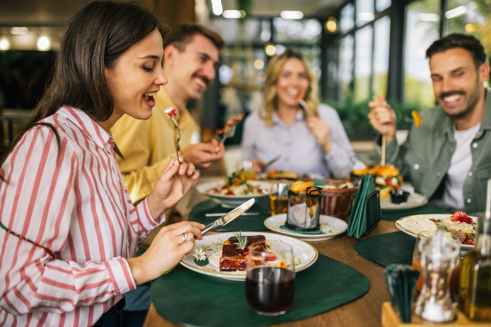 Group of happy friends eating lunch together in a restaurant. They eat delicious salads, hamburgers, bread and meat.