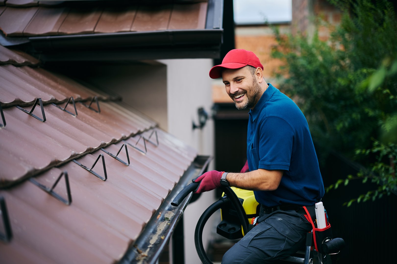 Happy man using leaf blower while cleaning gutters on the roof of a house. Copy space.