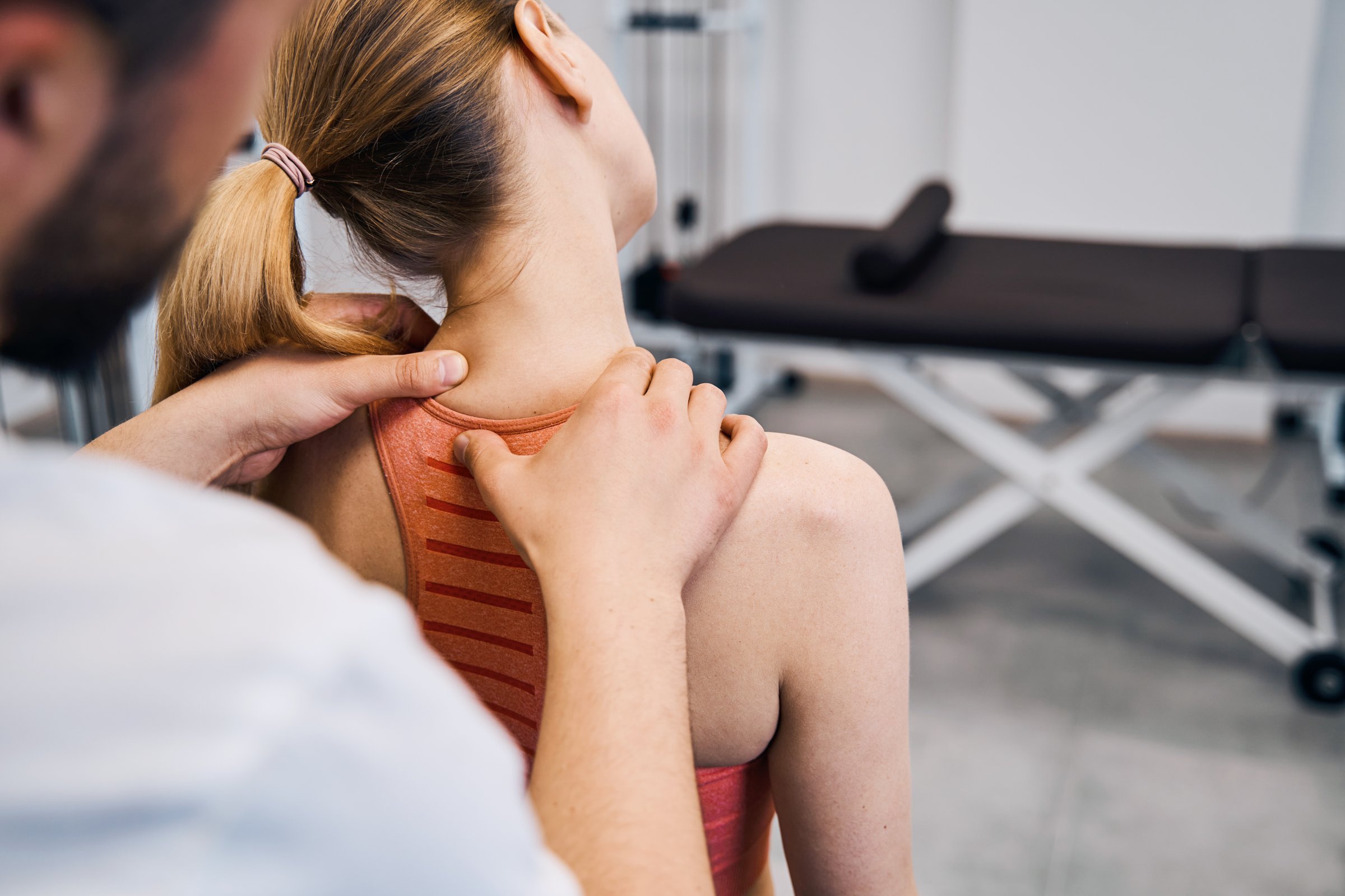 Physiotherapist hand massaging womans painful neck in physic room closeup back view. Male masseur making recovery therapy after sport injury in rehabilitation center. Chiropractic healthcare
