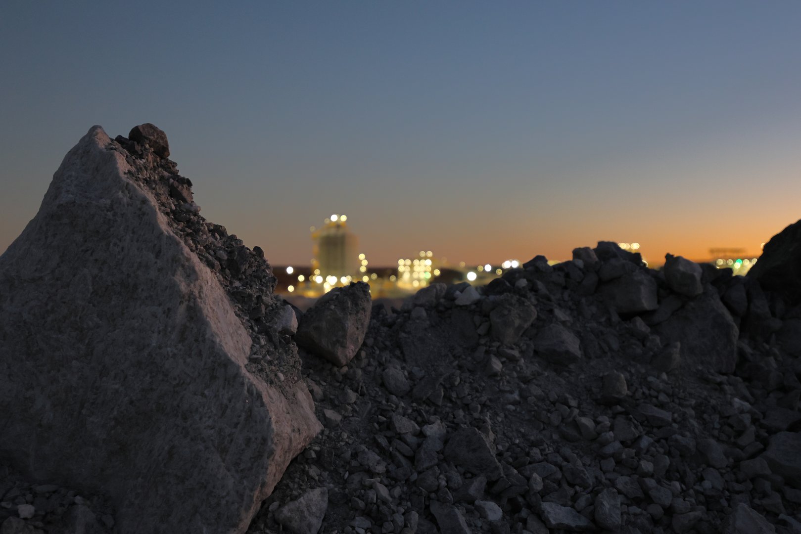 Mining, sunrise or sunset industry?  Twilight, blue hour at mine.  Lights of processing plant out of focus. Copy space in dark foreground or orange blue sky