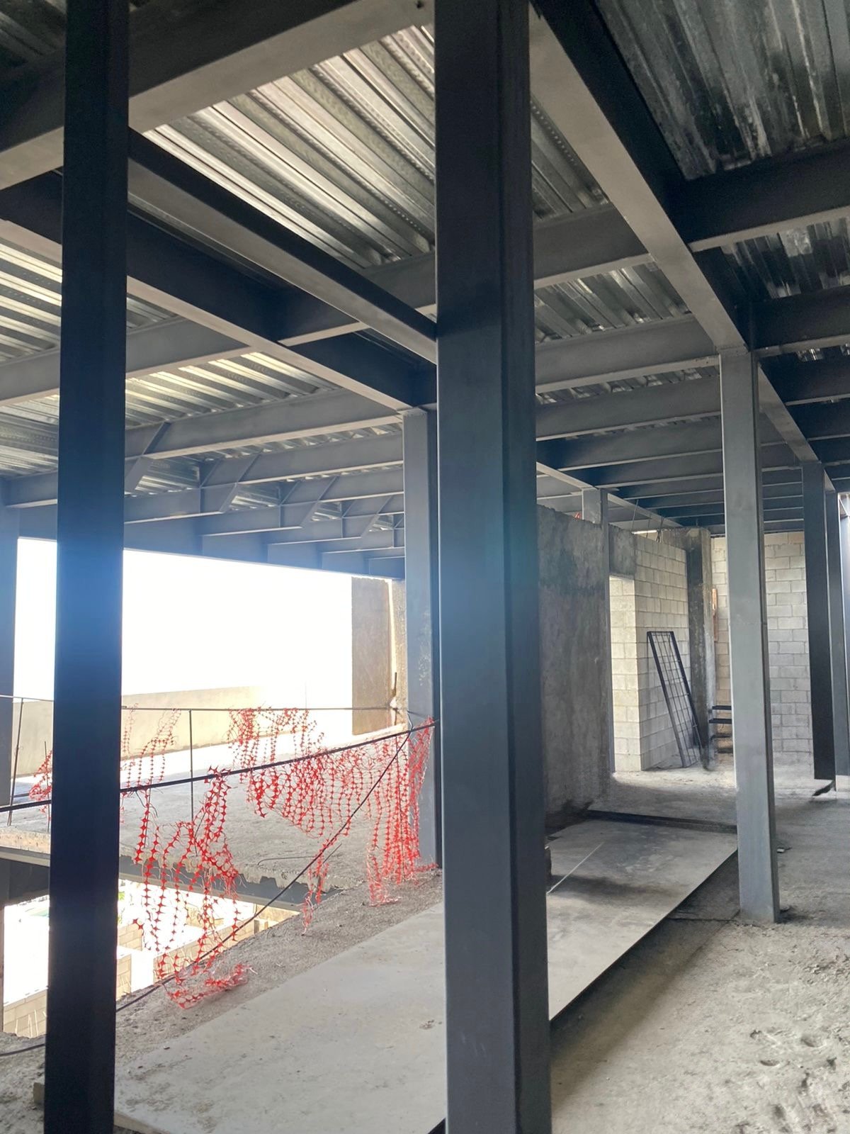 Construction site with metal framework, concrete slabs, and safety netting on the second floor of a building.