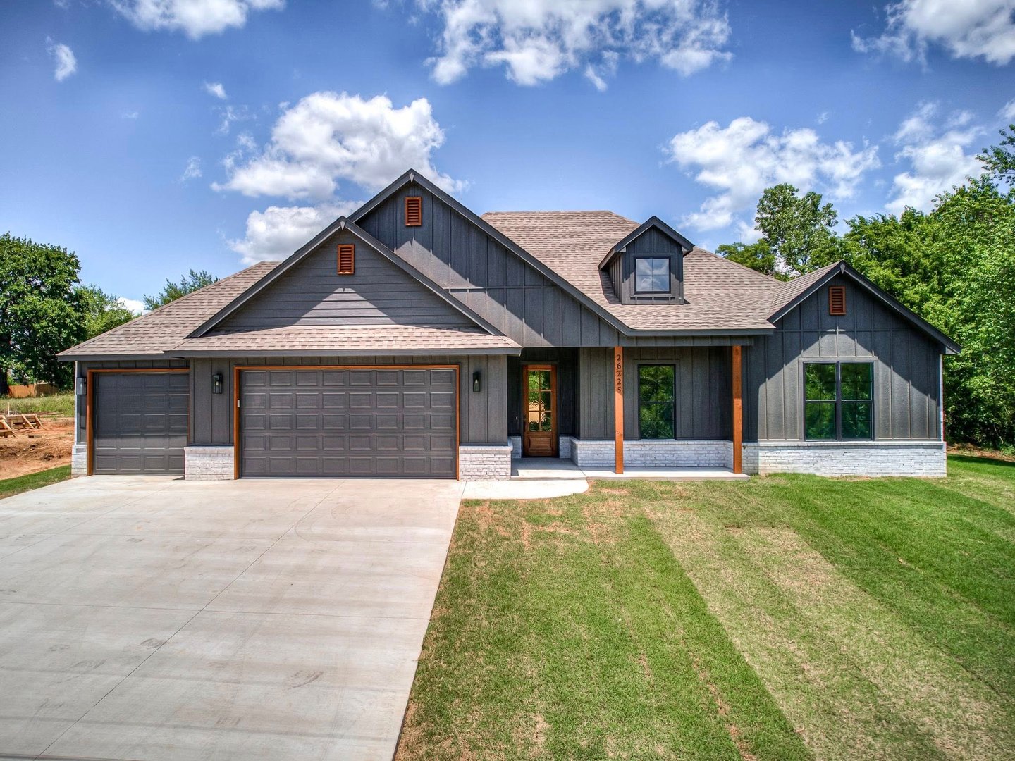 Modern luxury home exterior with large windows, stone facade, and spacious driveway at sunset.