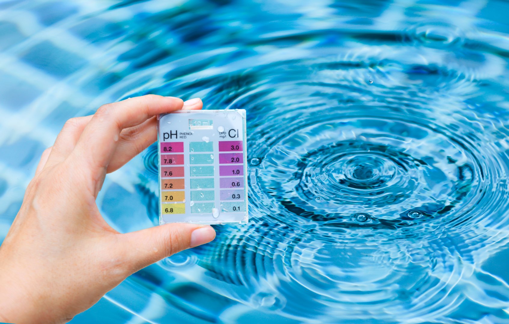 Pool tester test kit in girl hand over water background, water quality testing, quality test kit for swimming pool water
