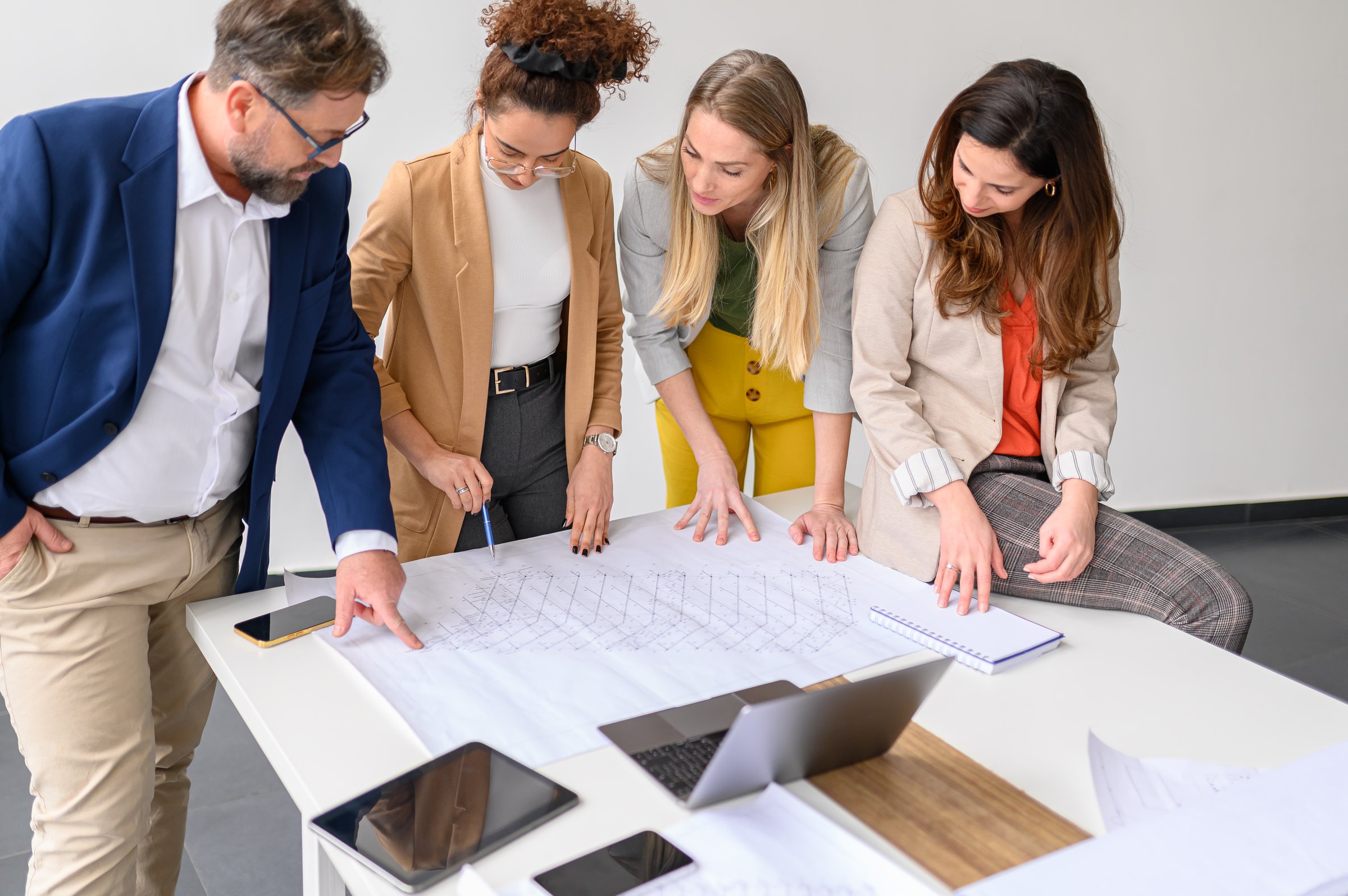 Business people examining blueprint and working on new project with computer and mobile phones on table in office
