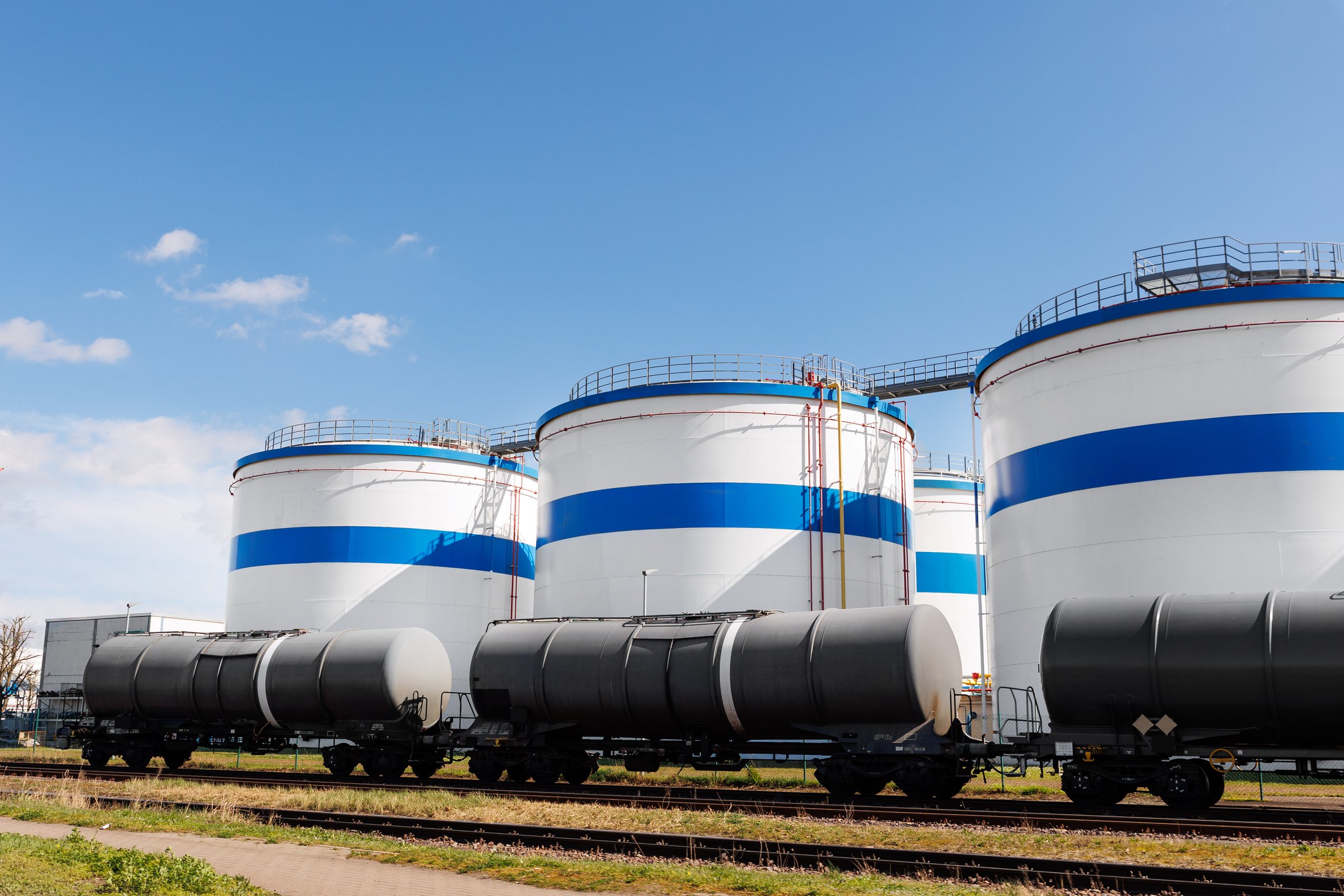 Row many large industrial fuel storage white tanks clear blue sky background on sunny day. Oil storage refinery depot liquid facilities. Energy hazmat railroad transportation storage and distribution.