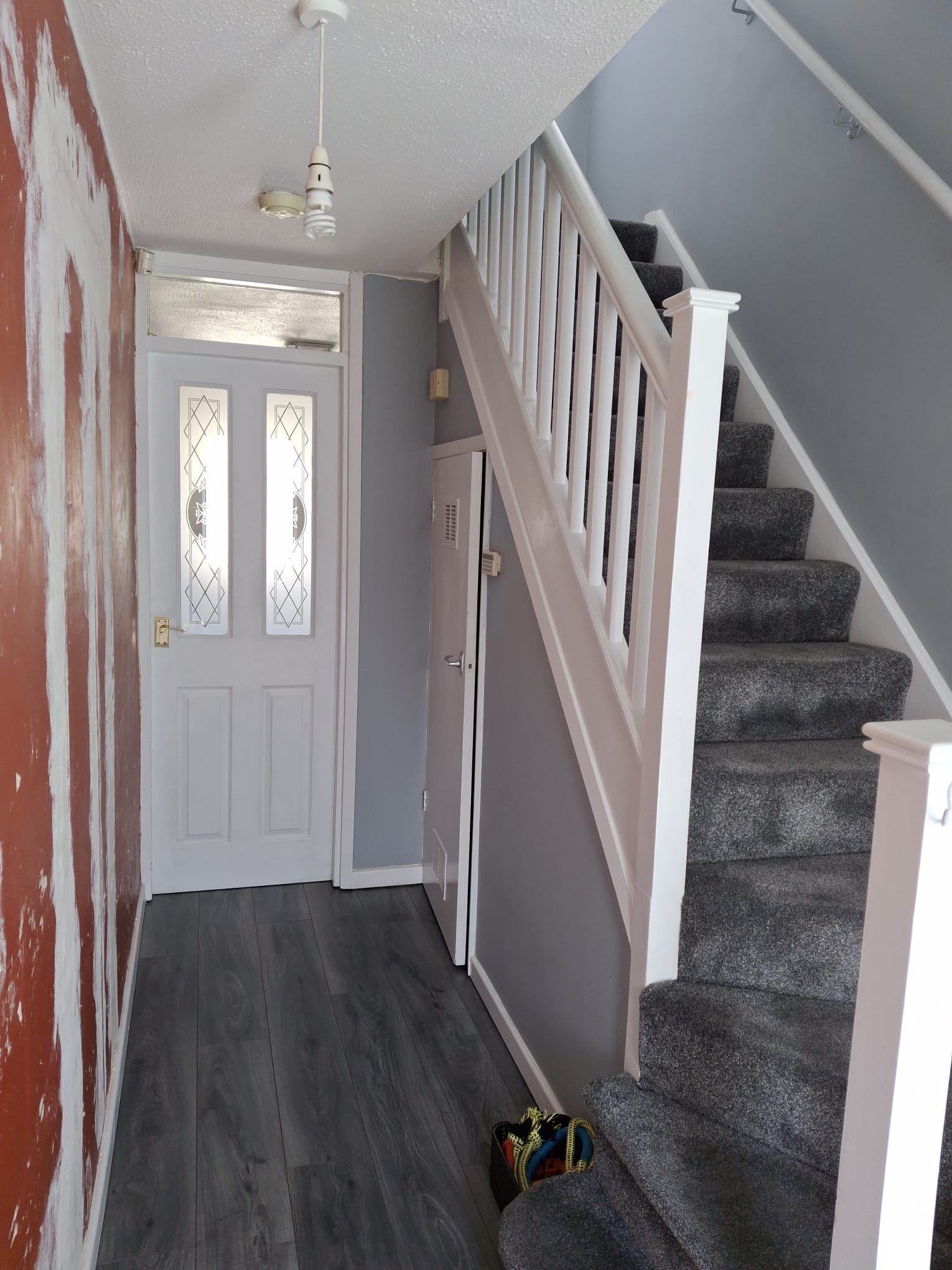 Interior of a hallway with gray walls, carpeted stairs, wooden flooring, and a partially painted wall.