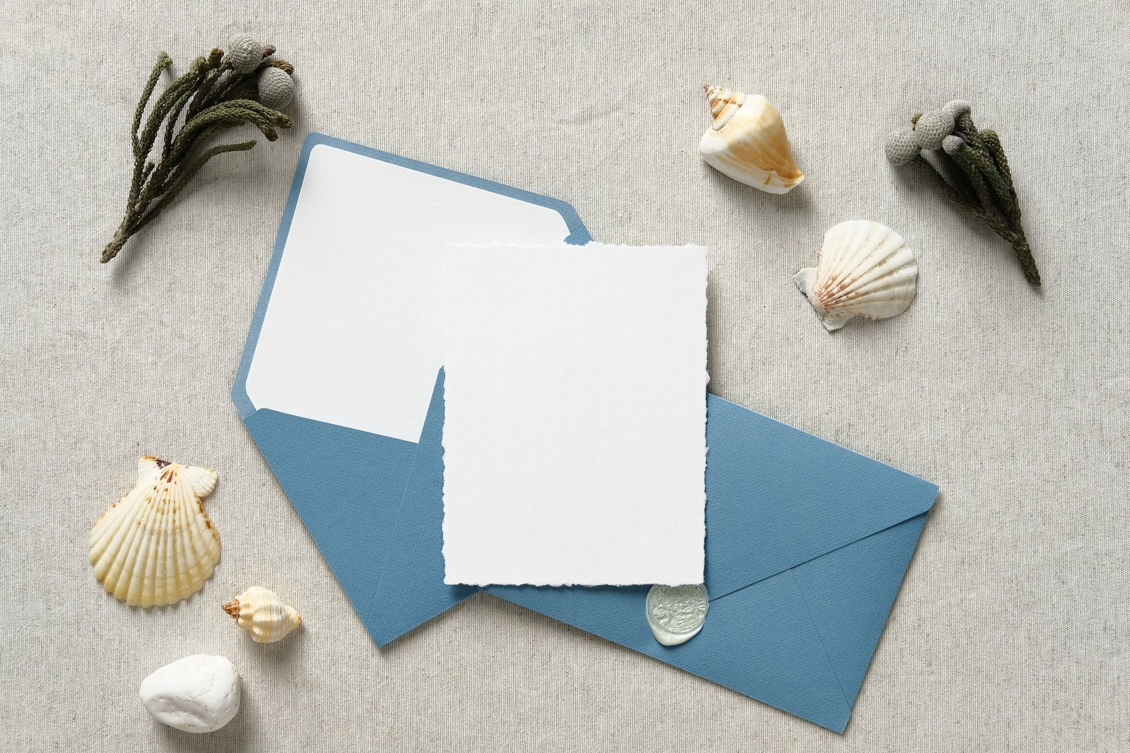 Nautical wedding invitation card mockup with blue envelopes, flowers, seashell on beige table. Flat lay, top view, copy space.