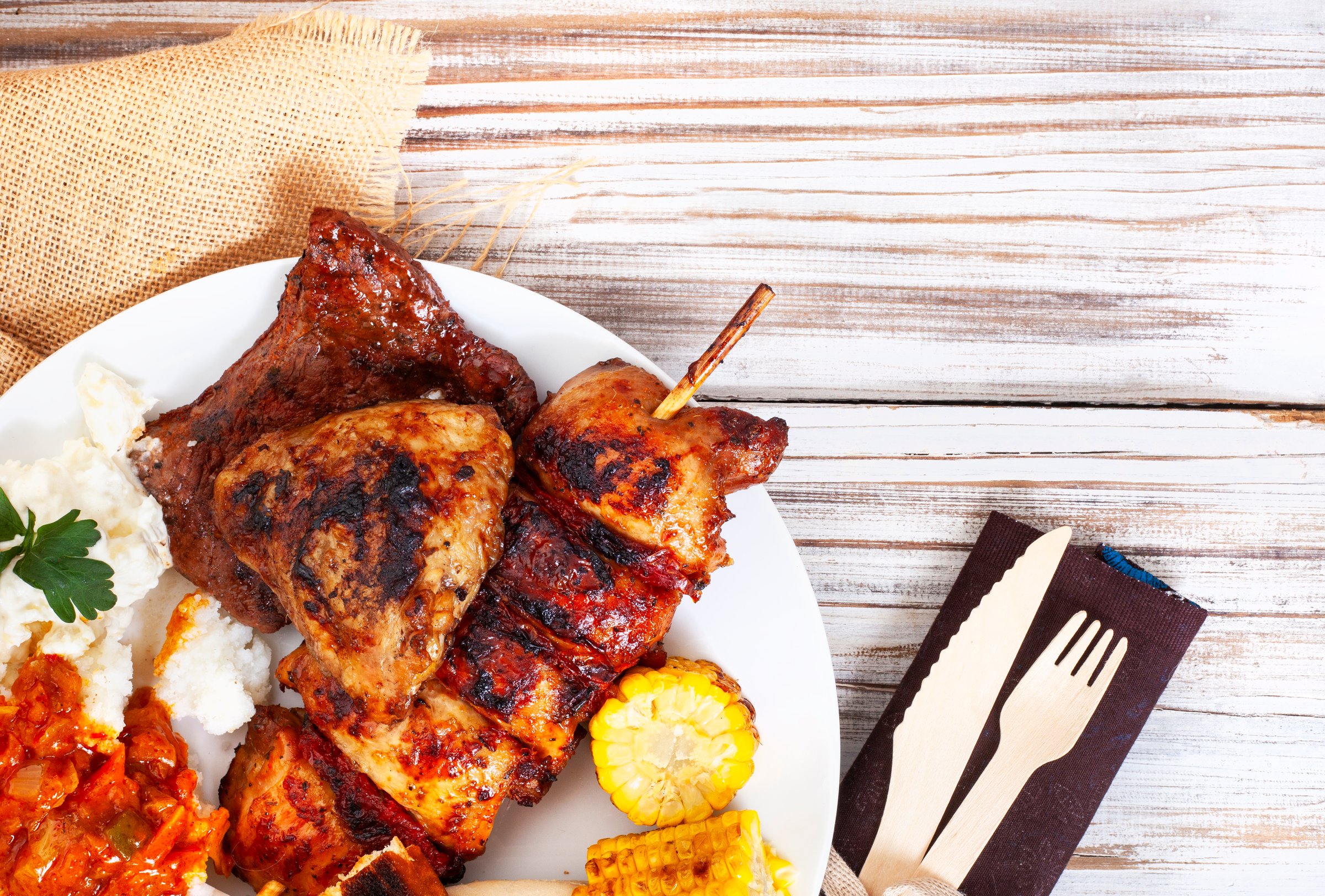 Flat lay of a plate of traditional South African braai food, rustic table setting and copy space on right