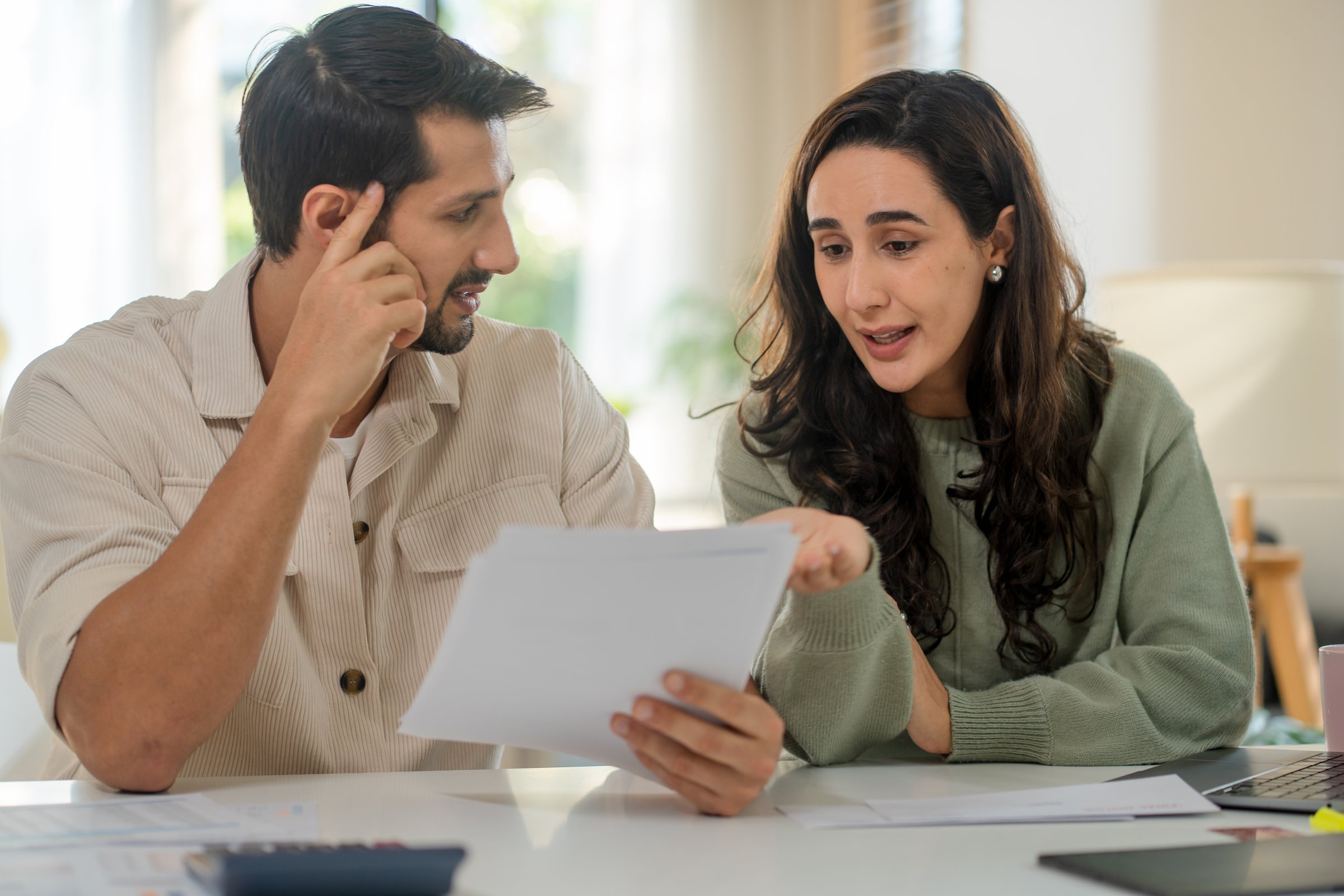 Couple supports one another while reading paperwork and calculating expenses, aiming for financial stability amidst inflation and economic pressure.