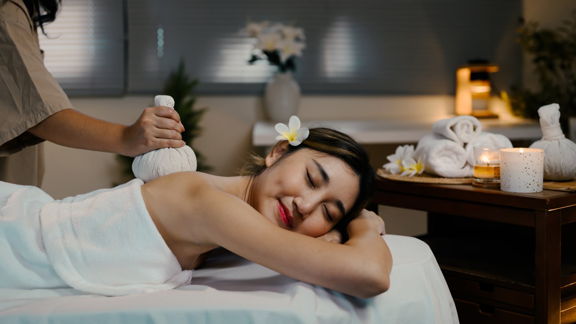 Relaxed woman receiving traditional herbal compress massage in a serene spa.