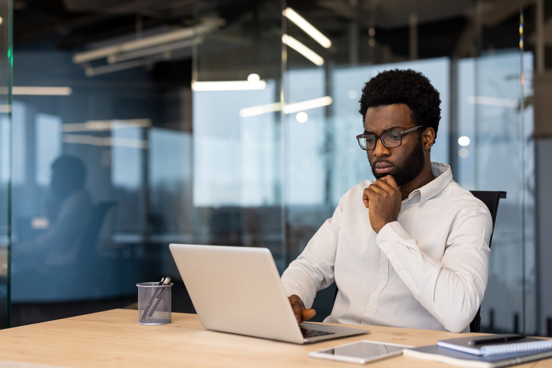 African American businessman thinking laptop work. Capturing thoughtful expression, business attire, office ambiance. Represents focus, technology usage, corporate environment, decision making.