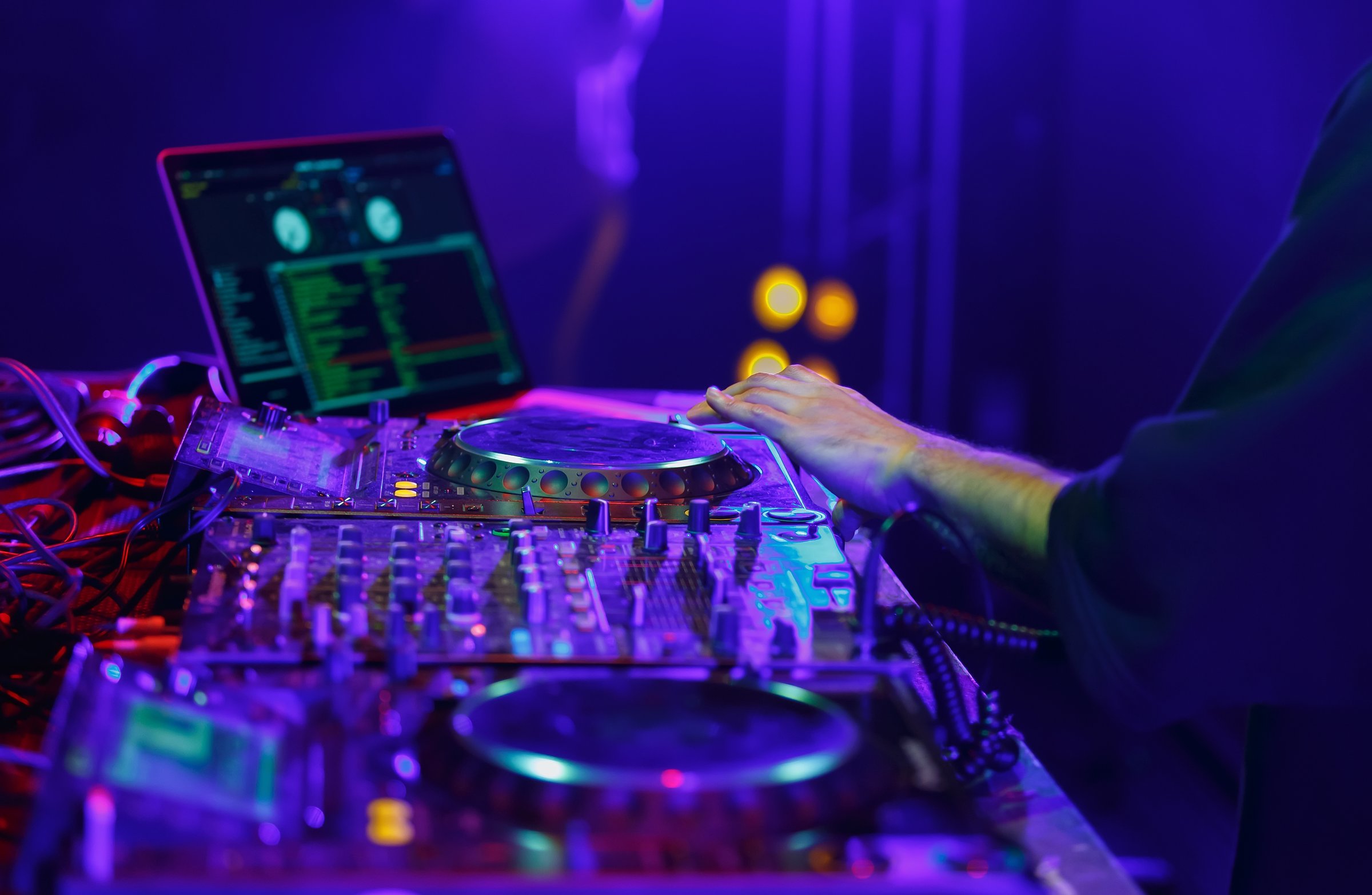 Disc jockey performing on stage in night club. Professional DJ plays set with CD turntables, sound mixer and laptop computer
