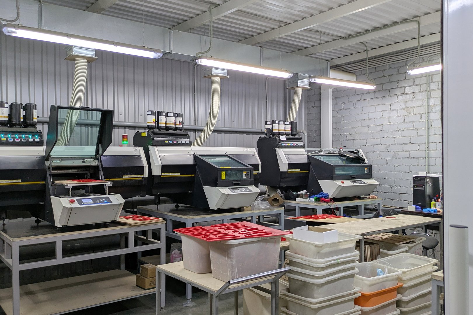 Industrial workshop with modern UV printers set up for production, is equipped with ventilation systems and work tables with pallets filled with red painted wooden parts